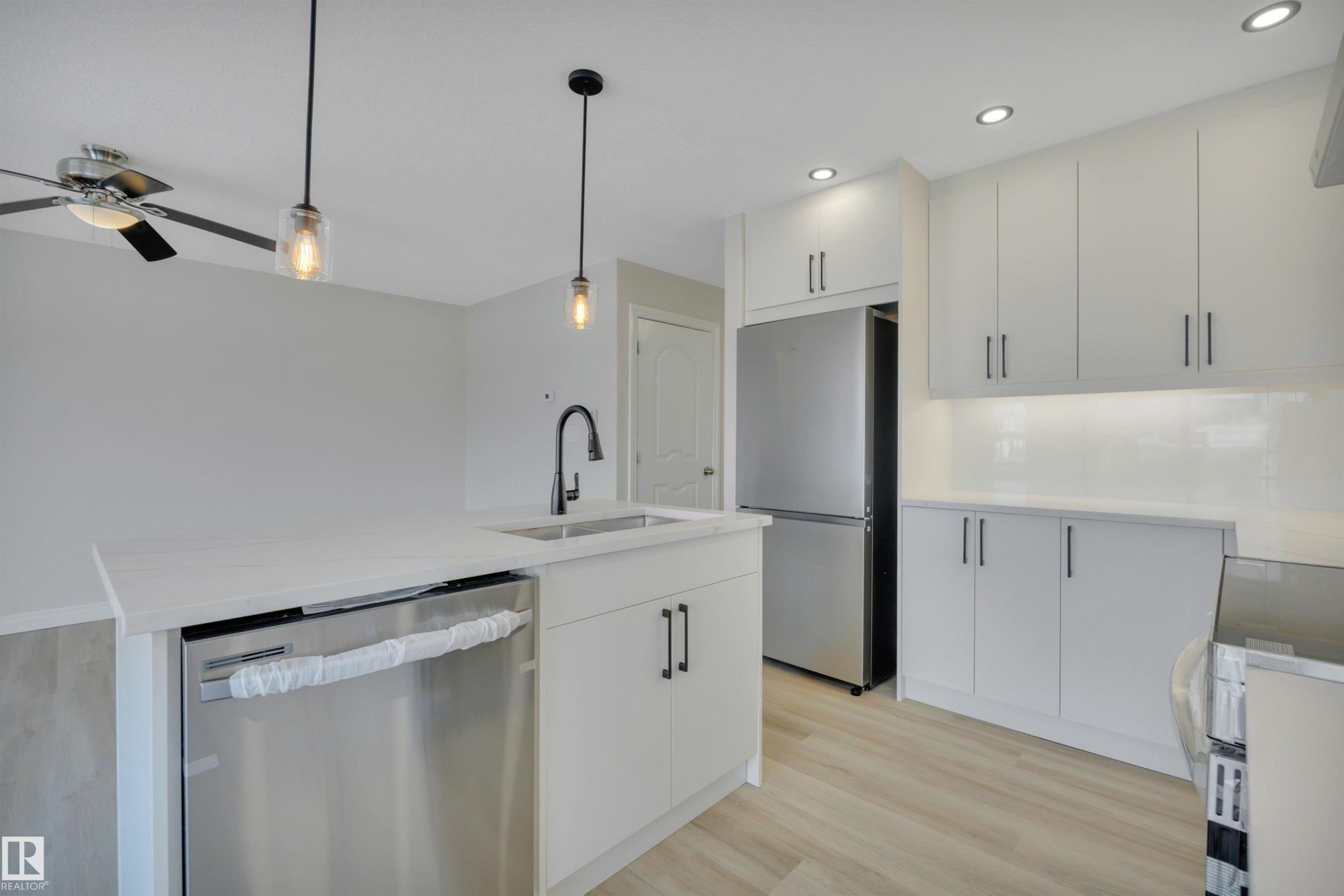 Kitchen featuring appliances with stainless steel finishes, light wood-type flooring, decorative light fixtures, an island with sink, and light stone counters - 457 Aster Close, Leduc, AB - Indoor Photo Showing Kitchen