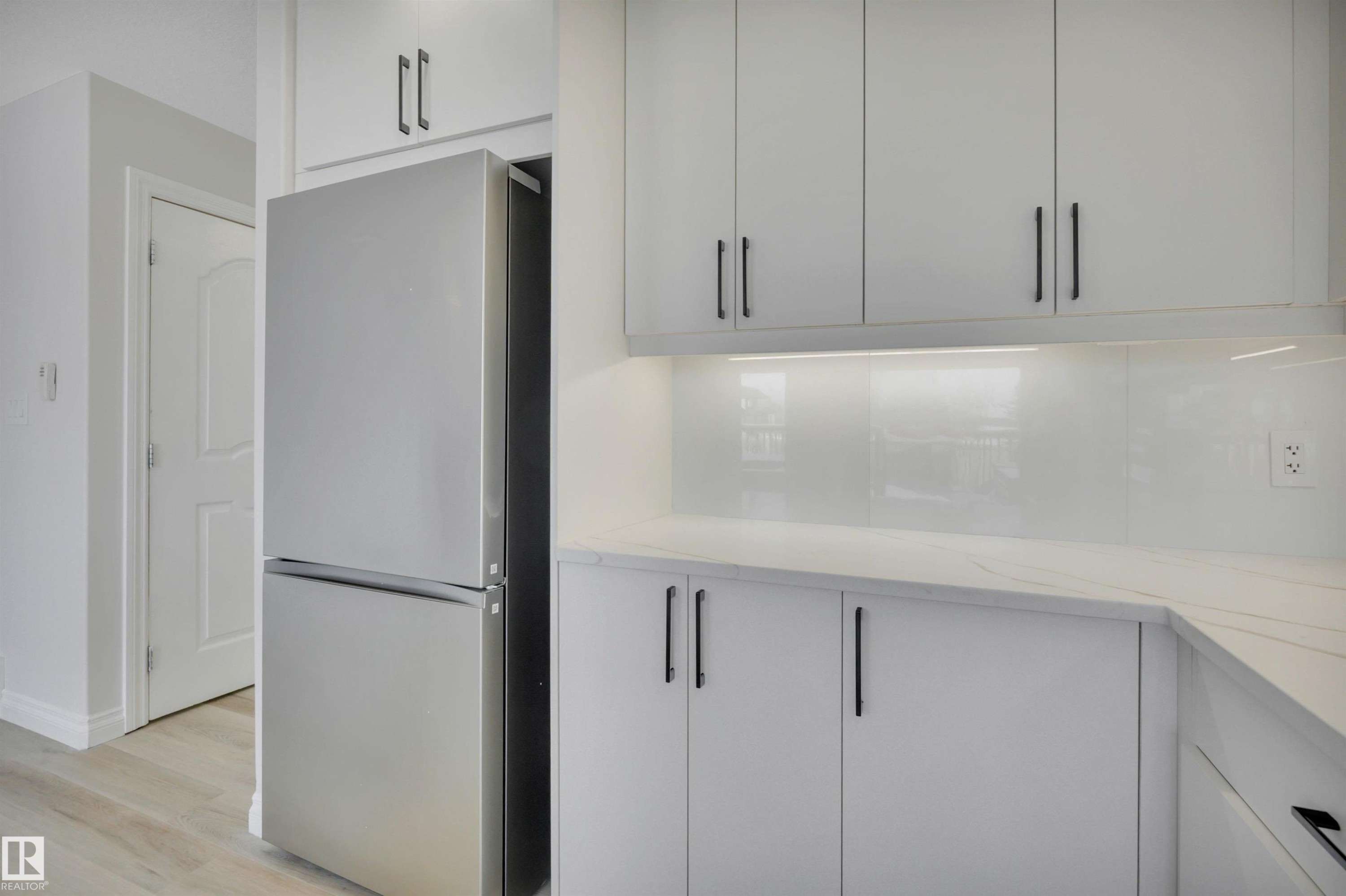 Kitchen featuring freestanding refrigerator, light stone countertops, light wood-style floors, and modern cabinets - 457 Aster Close, Leduc, AB - Indoor Photo Showing Kitchen