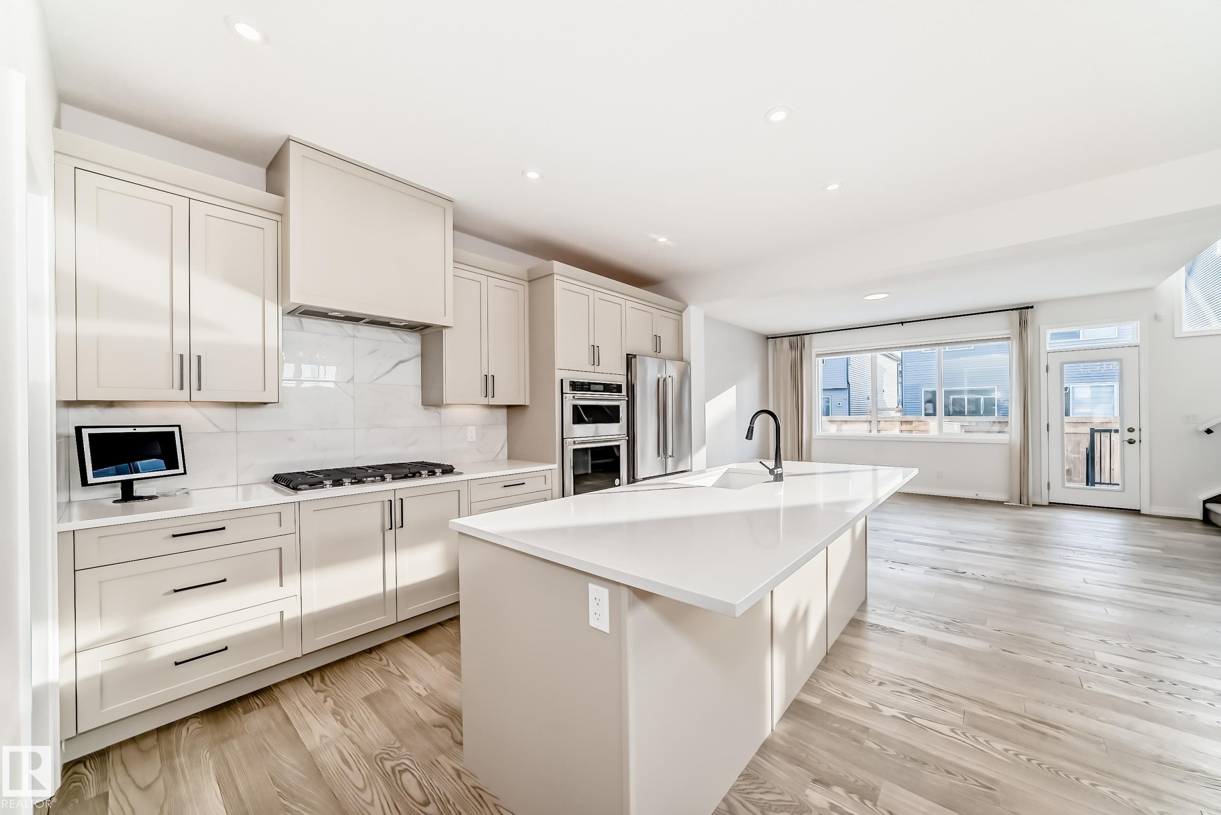 Kitchen with an island with sink, light wood-type flooring, tasteful backsplash, appliances with stainless steel finishes, and recessed lighting - 3249 Dixon Way, Edmonton, AB - Indoor Photo Showing Kitchen With Upgraded Kitchen