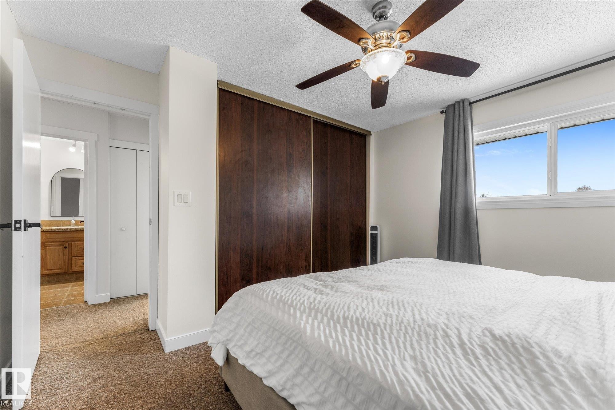 Carpeted bedroom featuring a textured ceiling, a closet, ceiling fan, and ensuite bathroom - 289 Grandin Village, St. Albert, AB - Indoor Photo Showing Bedroom