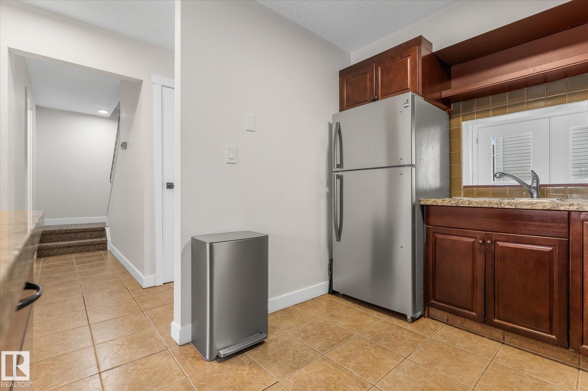 Kitchen with freestanding refrigerator, light stone countertops, light tile patterned floors, and a textured ceiling - 289 Grandin Village, St. Albert, AB - Indoor Photo Showing Kitchen
