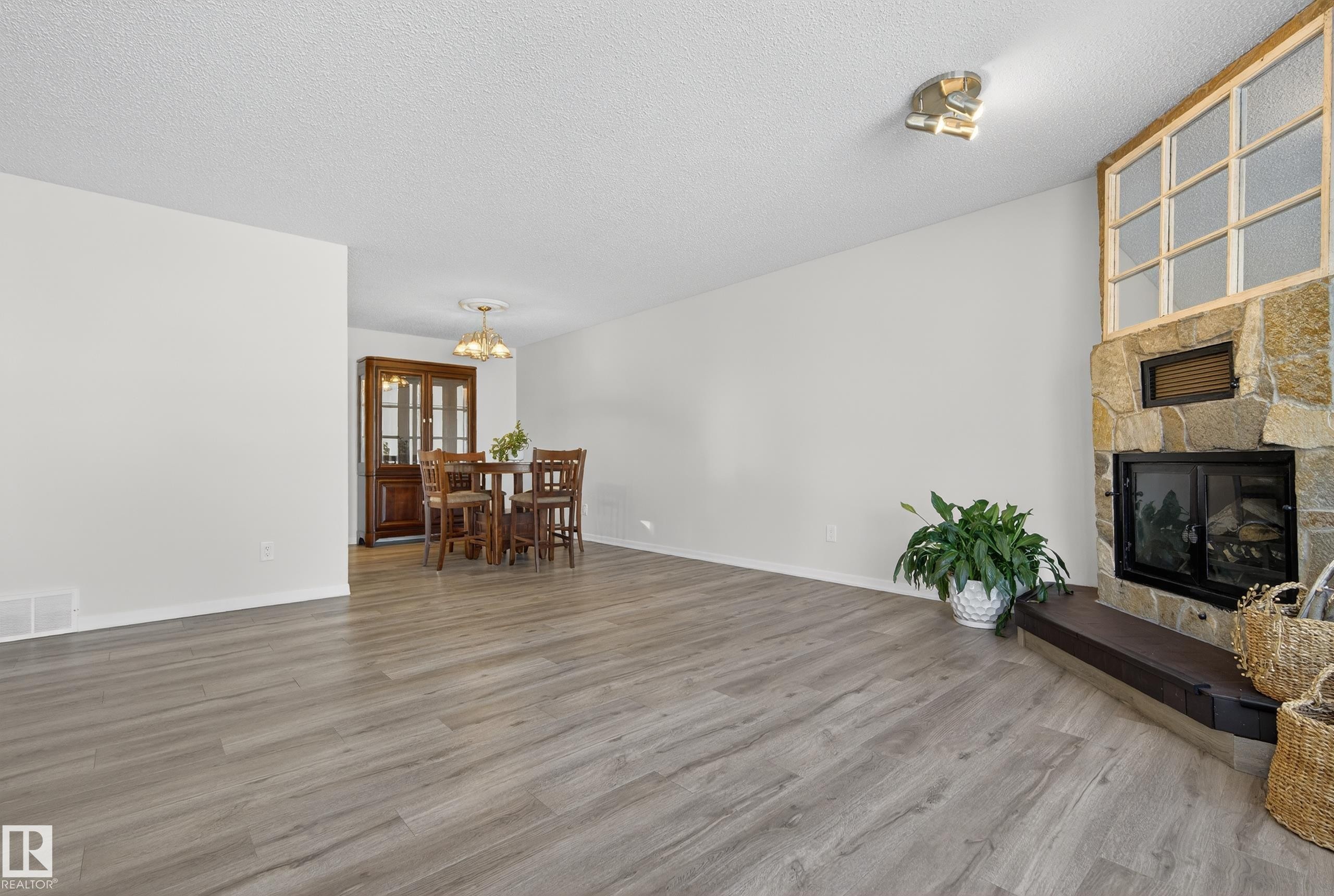 Living room with light wood-style flooring, a stone fireplace, a textured ceiling, and a chandelier - 1704 89 Street, Edmonton, AB - Indoor Photo Showing Living Room With Fireplace