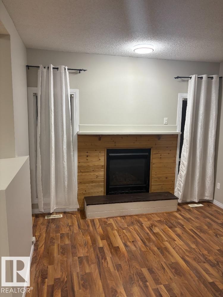 Unfurnished living room featuring a fireplace with raised hearth, dark wood finished floors, and a textured ceiling - 24 3812 20 Avenue, Edmonton, AB - Indoor With Fireplace