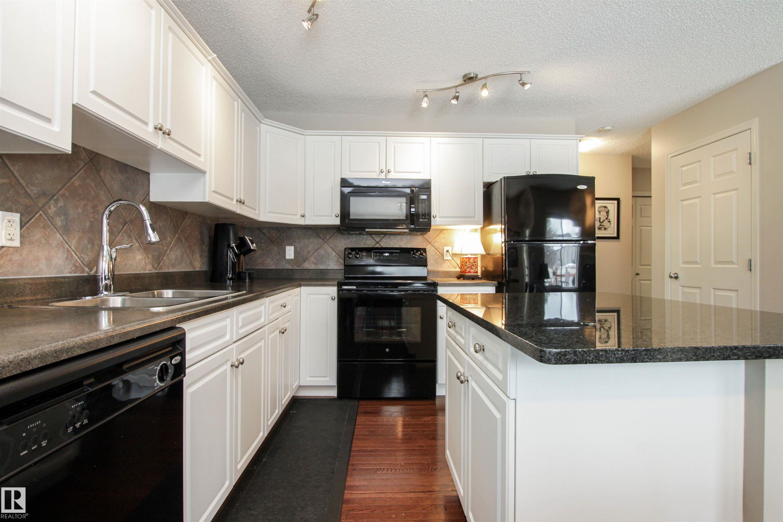 Kitchen with black appliances, white cabinetry, dark wood finished floors, a kitchen island, and a textured ceiling - 2315 Lemieux Place, Edmonton, AB - Indoor Photo Showing Kitchen With Double Sink