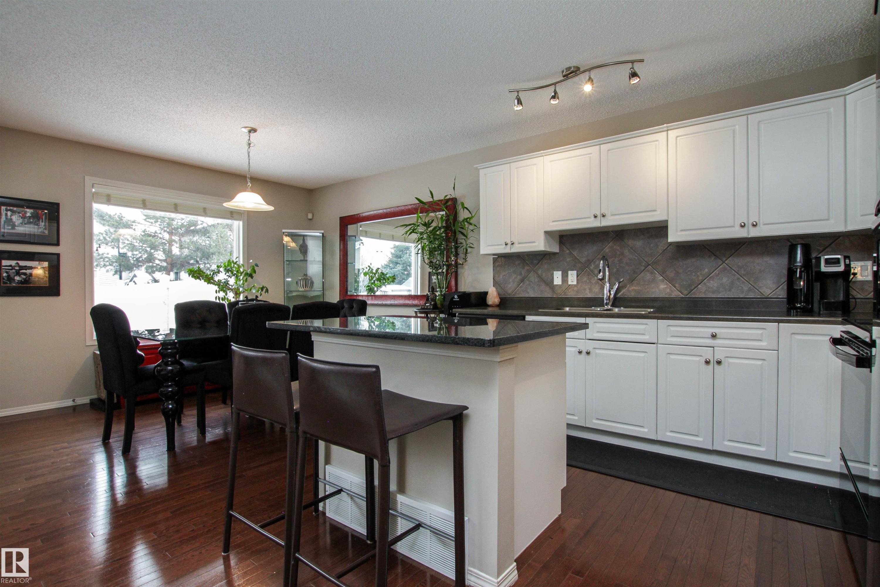 Kitchen with a center island, white cabinets, dark wood-type flooring, a kitchen breakfast bar, and decorative light fixtures - 2315 Lemieux Place, Edmonton, AB - Indoor