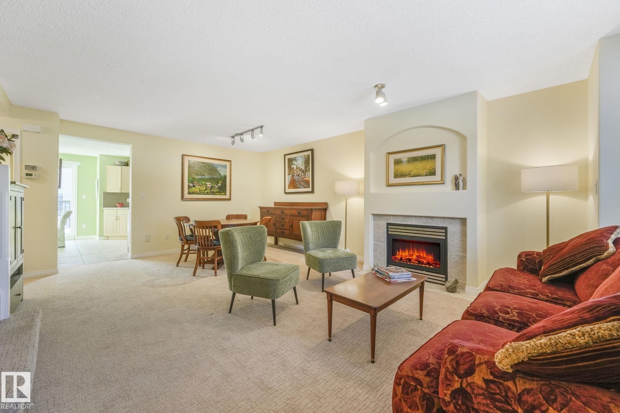 Living area with a tile fireplace, light carpet, rail lighting, and a textured ceiling - 23 4755 Terwillegar Common, Edmonton, AB - Indoor Photo Showing Living Room With Fireplace