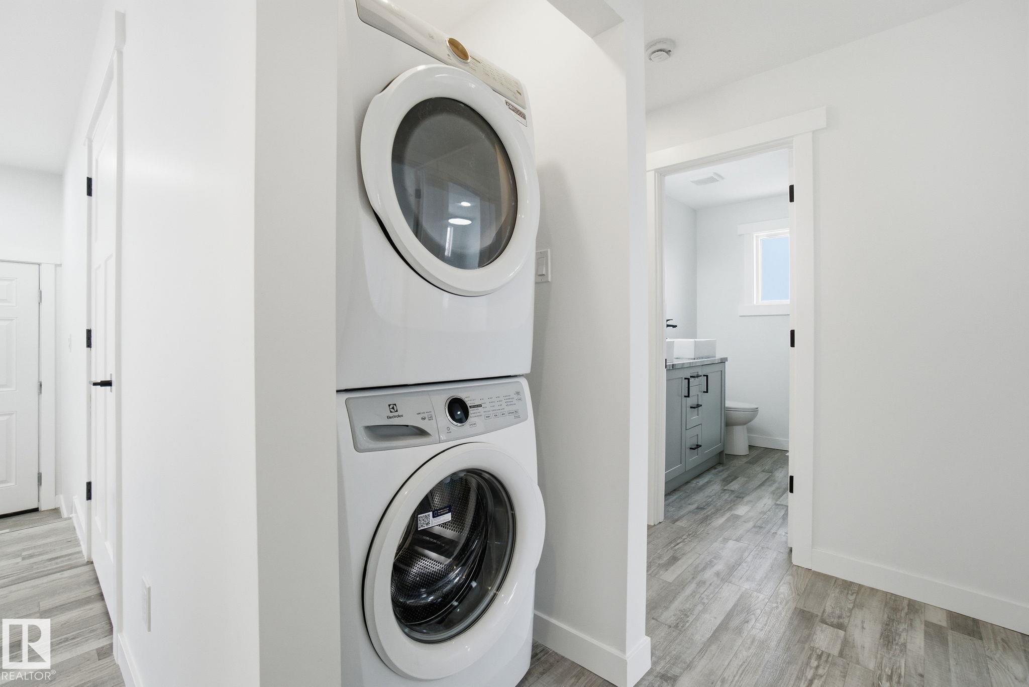 Laundry area featuring light wood-type flooring and stacked washer and clothes dryer - 7112 132 Avenue, Edmonton, AB - Indoor Photo Showing Laundry Room