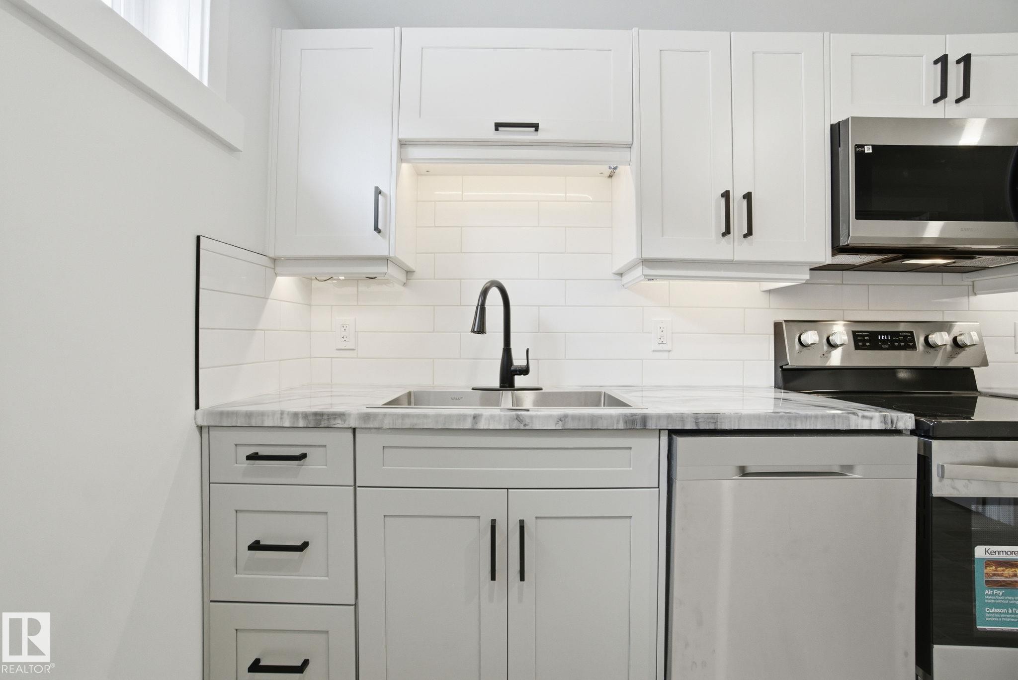 Kitchen with appliances with stainless steel finishes, white cabinetry, light stone countertops, and decorative backsplash - 7112 132 Avenue, Edmonton, AB - Indoor Photo Showing Kitchen With Upgraded Kitchen