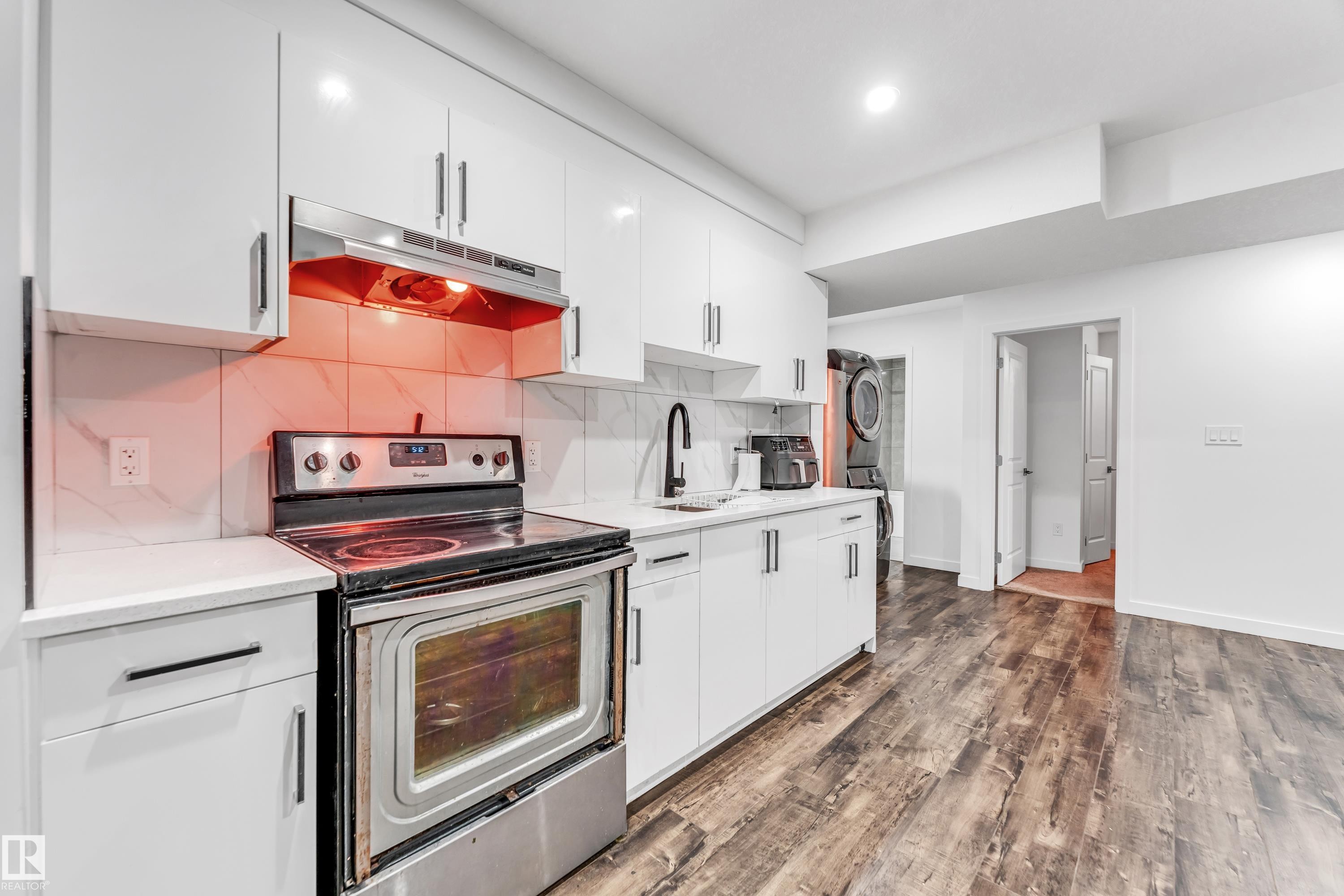 Kitchen featuring electric range, under cabinet range hood, white cabinetry, stacked washer / dryer, and dark wood finished floors - 2095 Maple Road, Edmonton, AB - Indoor Photo Showing Kitchen