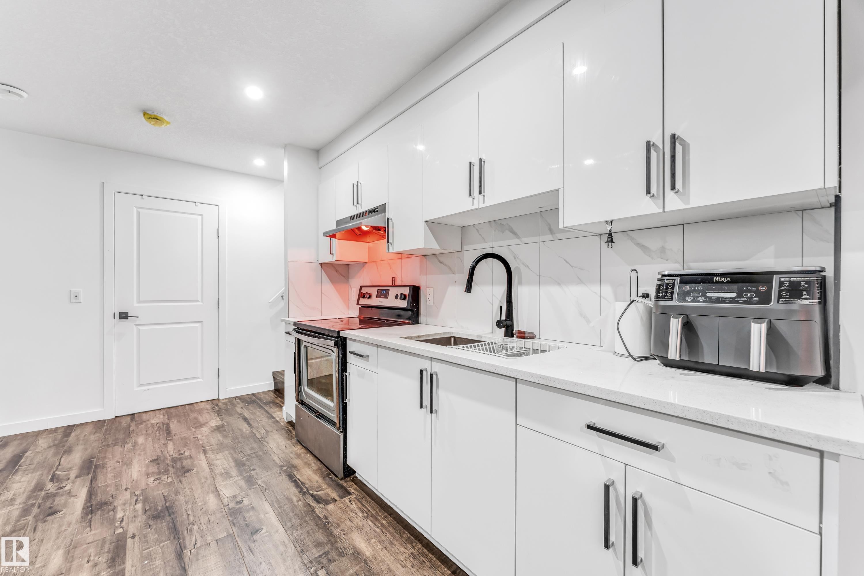 Kitchen with electric stove, white cabinets, dark wood-style flooring, light stone countertops, and tasteful backsplash - 2095 Maple Road, Edmonton, AB - Indoor Photo Showing Kitchen