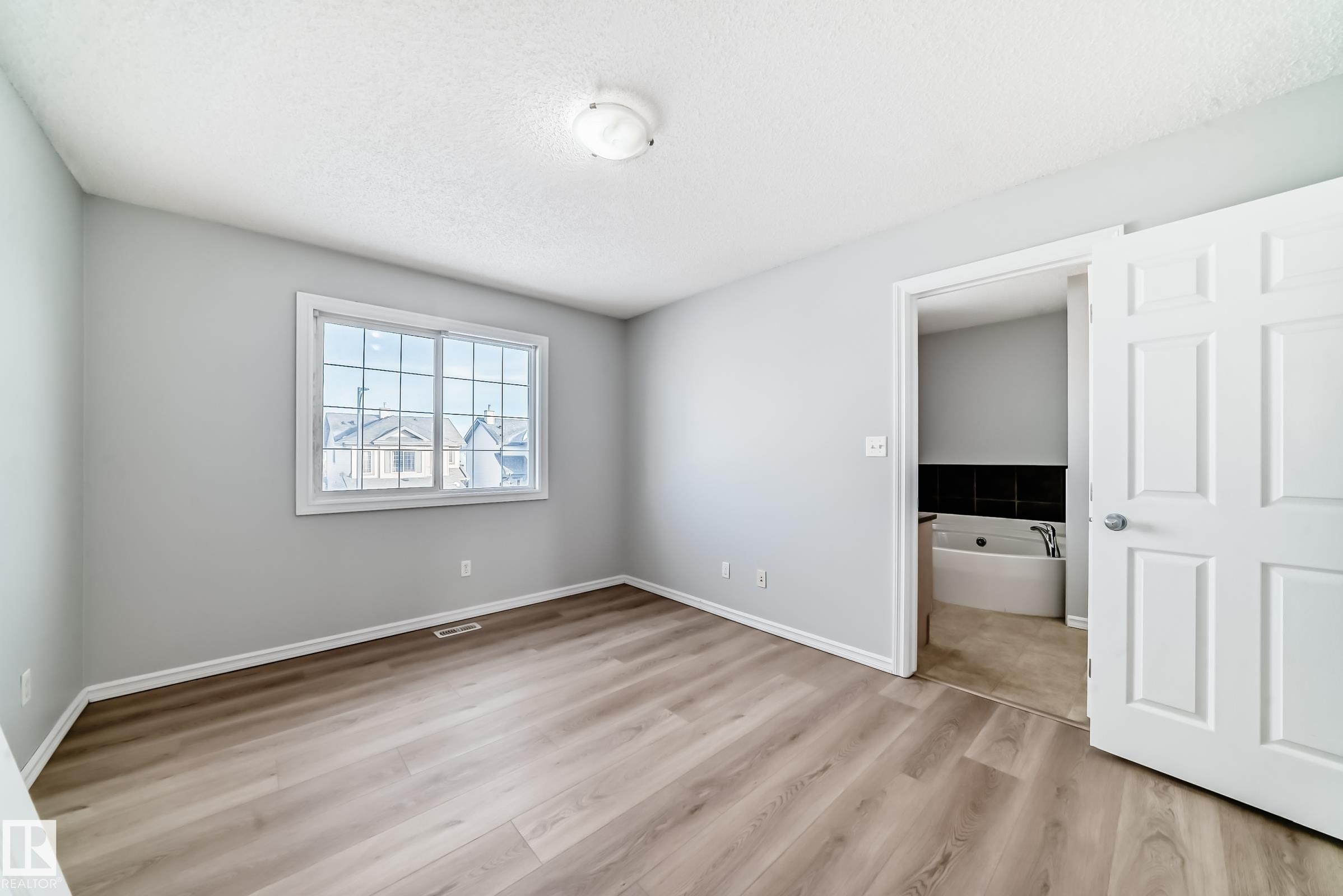 Unfurnished bedroom featuring light wood-type flooring, a textured ceiling, and connected bathroom - 7731 8 Avenue, Edmonton, AB - Indoor Photo Showing Other Room