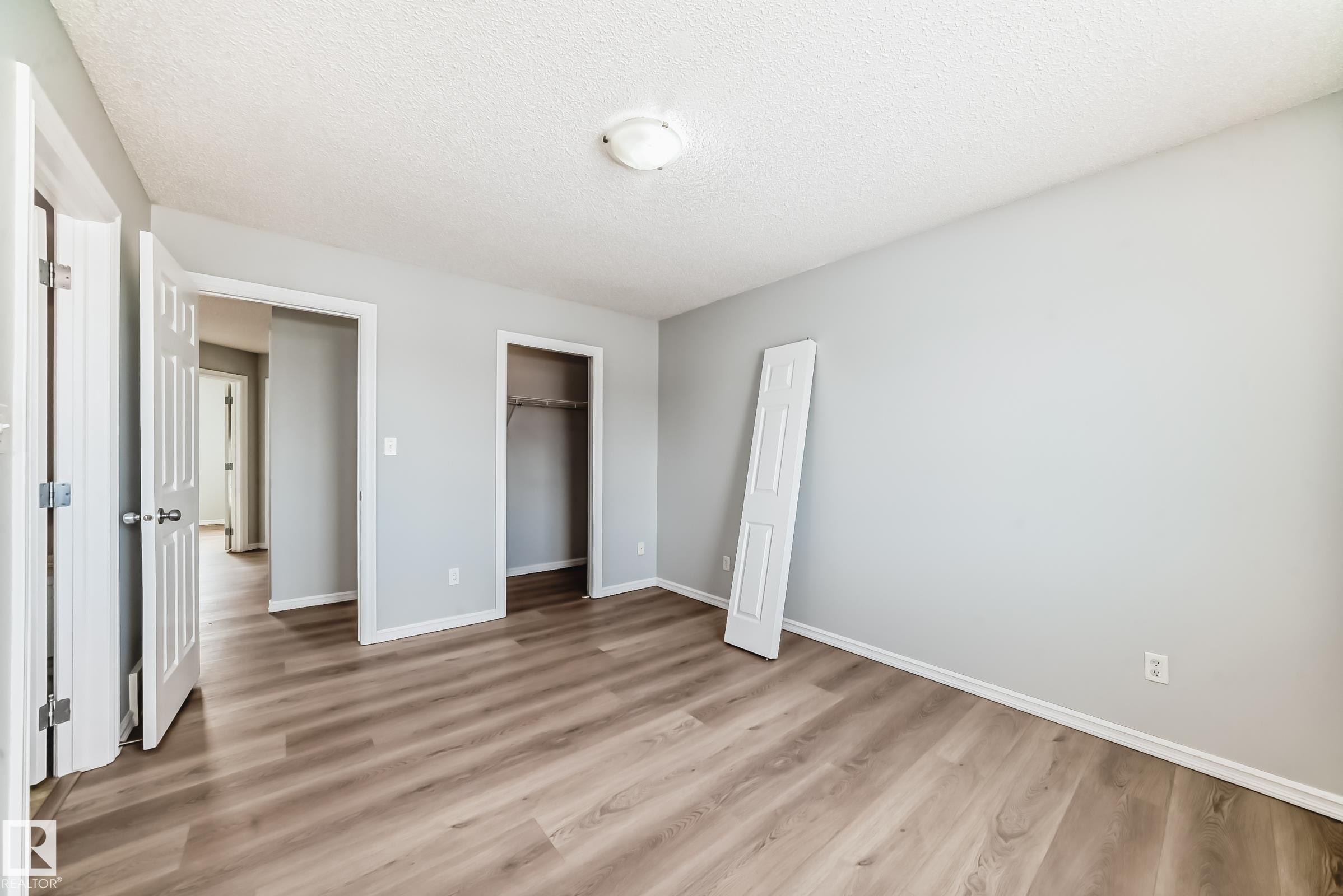 Unfurnished bedroom with a textured ceiling, light wood-style flooring, and a closet - 7731 8 Avenue, Edmonton, AB - Indoor Photo Showing Other Room