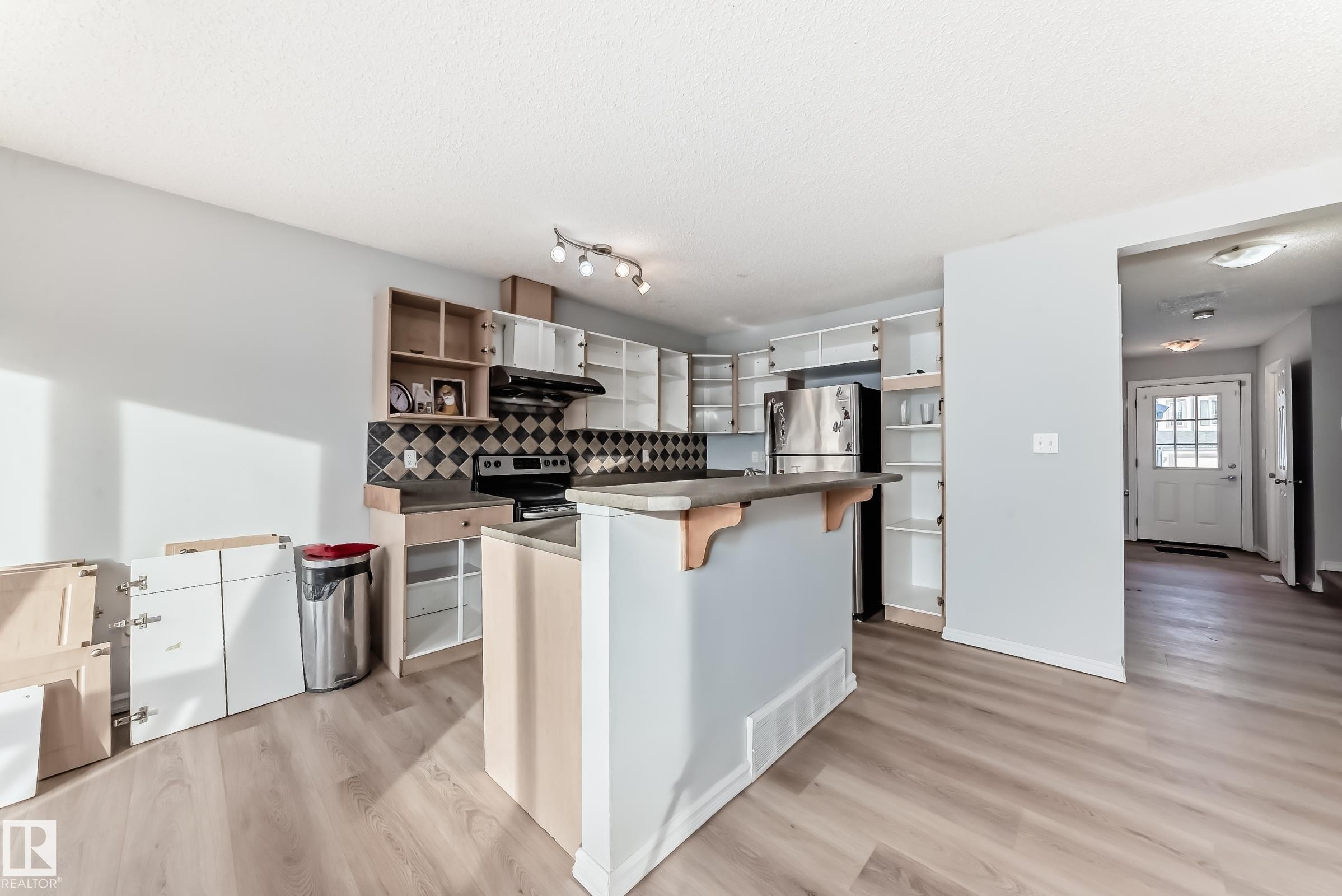 Kitchen with a breakfast bar, open shelves, light wood-style flooring, backsplash, and a textured ceiling - 7731 8 Avenue, Edmonton, AB - Indoor Photo Showing Kitchen