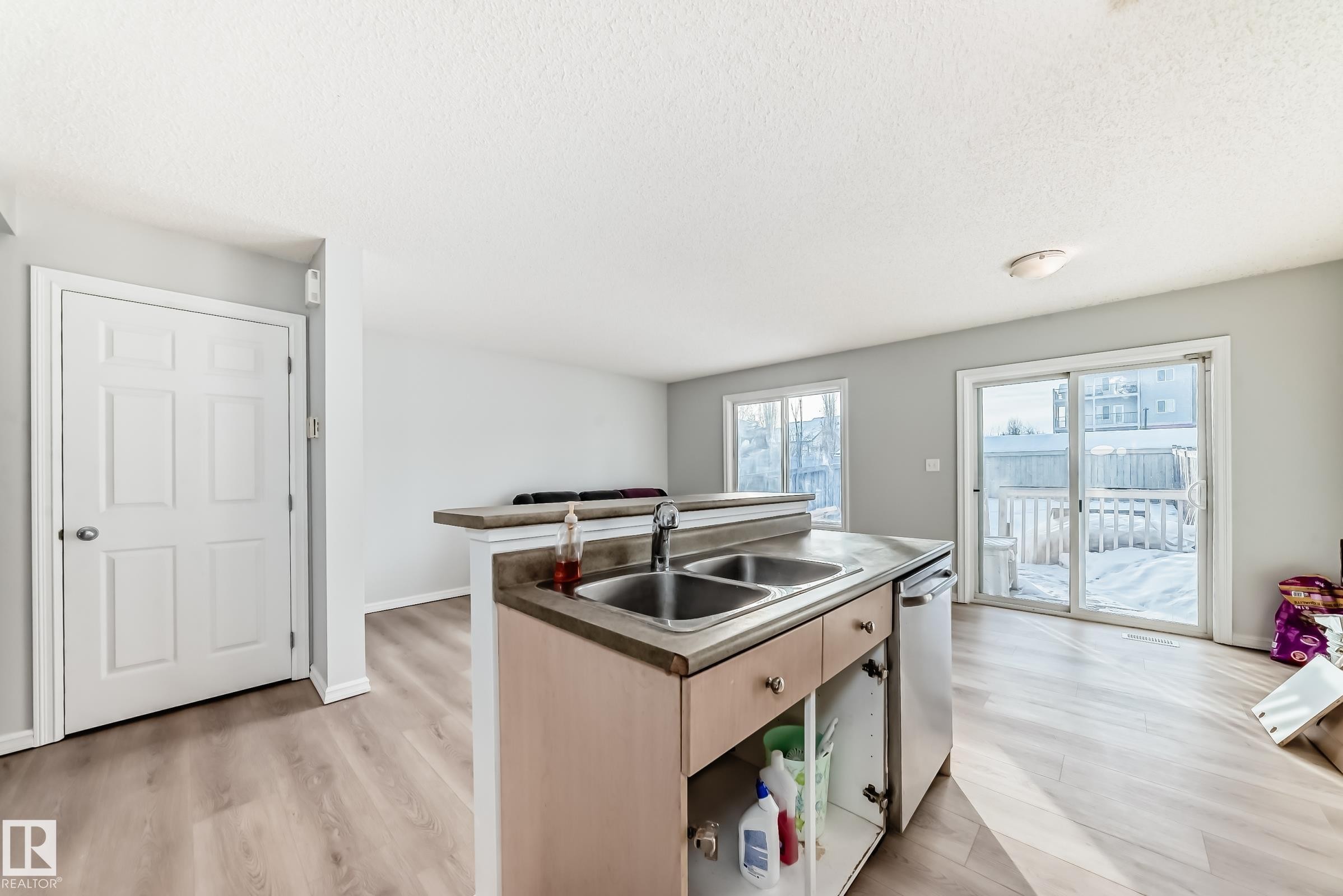 Kitchen featuring an island with sink, light wood-style floors, light brown cabinetry, dishwasher, and dark countertops - 7731 8 Avenue, Edmonton, AB - Indoor Photo Showing Kitchen With Double Sink