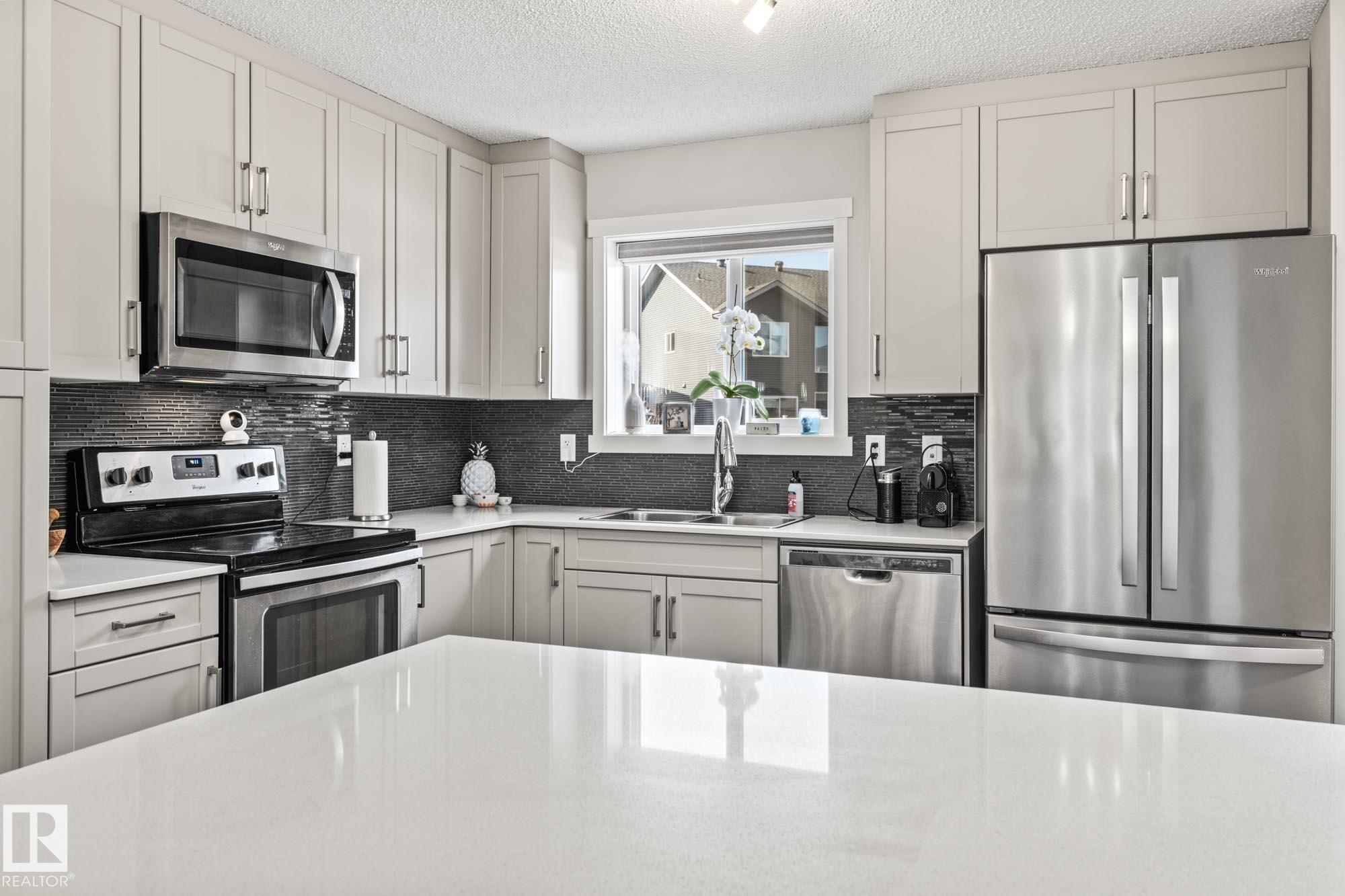 Kitchen featuring stainless steel appliances, light stone counters, a textured ceiling, and backsplash - 20110 27 Avenue, Edmonton, AB - Indoor Photo Showing Kitchen With Double Sink With Upgraded Kitchen
