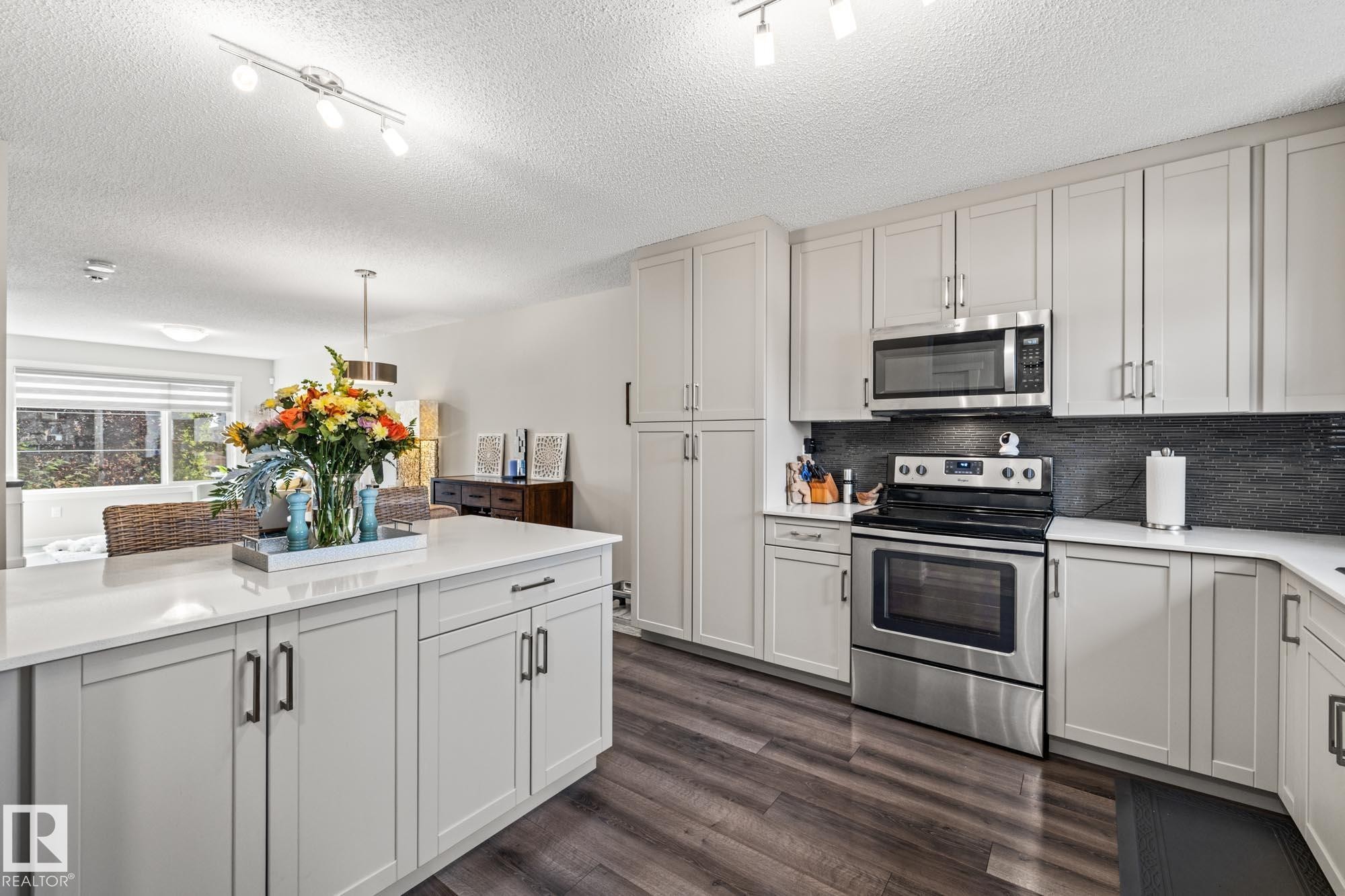 Kitchen featuring appliances with stainless steel finishes, dark wood finished floors, backsplash, track lighting, and a textured ceiling - 20110 27 Avenue, Edmonton, AB - Indoor Photo Showing Kitchen