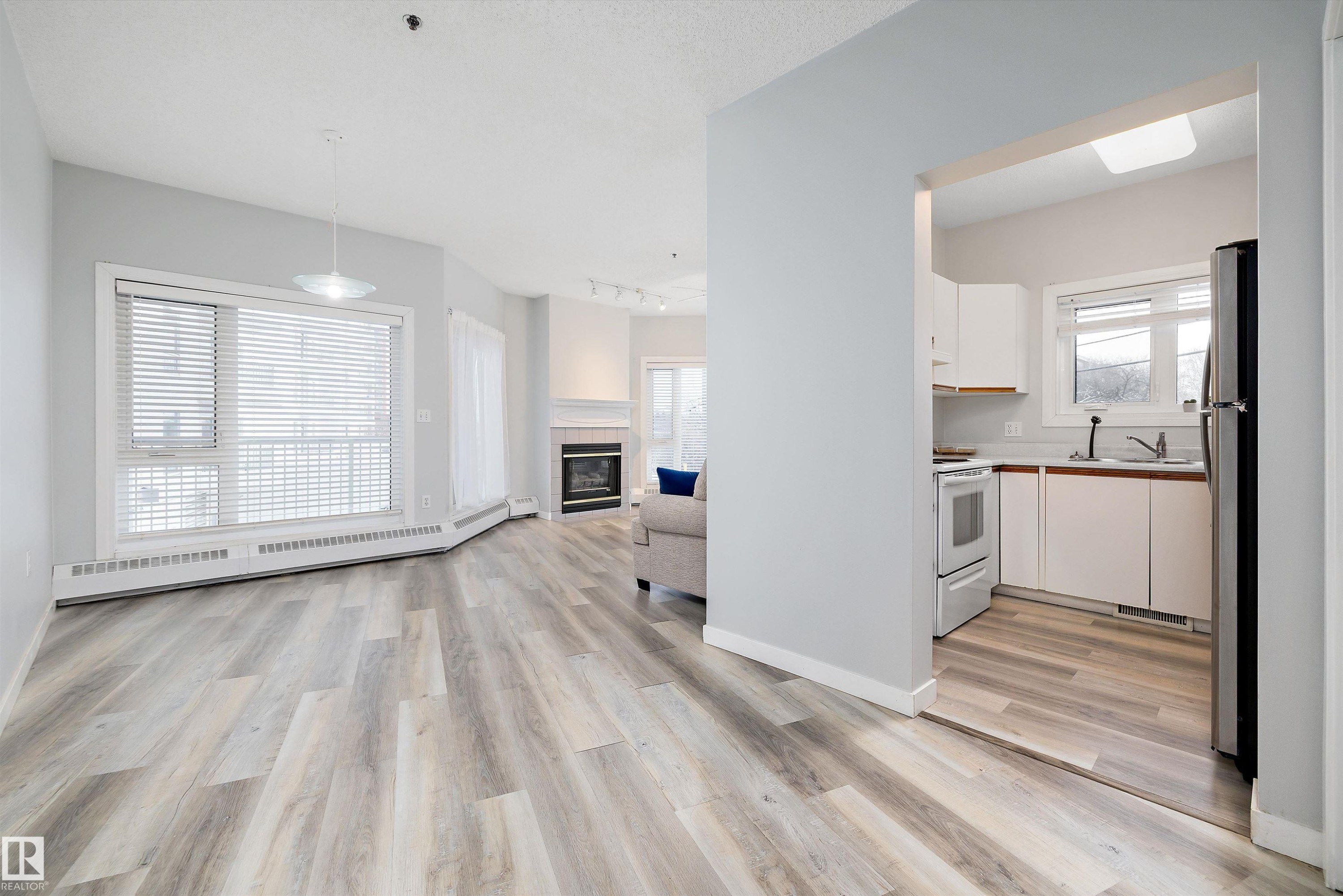 Kitchen featuring white cabinets, light countertops, baseboard heating, open floor plan, and a tiled fireplace - 205 10809 Saskatchewan Drive, Edmonton, AB - Indoor Photo Showing Other Room With Fireplace