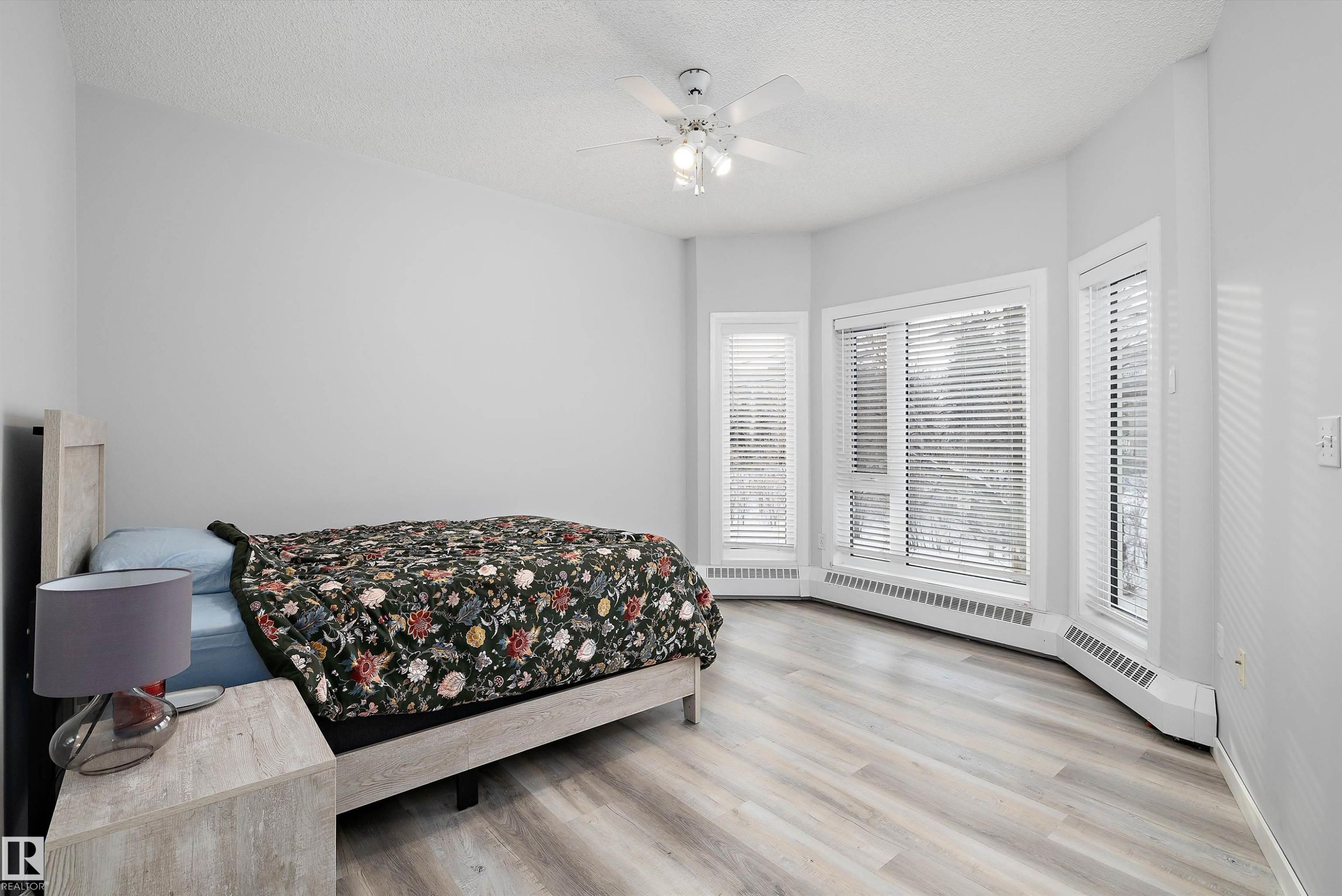 Bedroom featuring a textured ceiling, light wood-style flooring, ceiling fan, and a baseboard heating unit - 205 10809 Saskatchewan Drive, Edmonton, AB - Indoor Photo Showing Bedroom