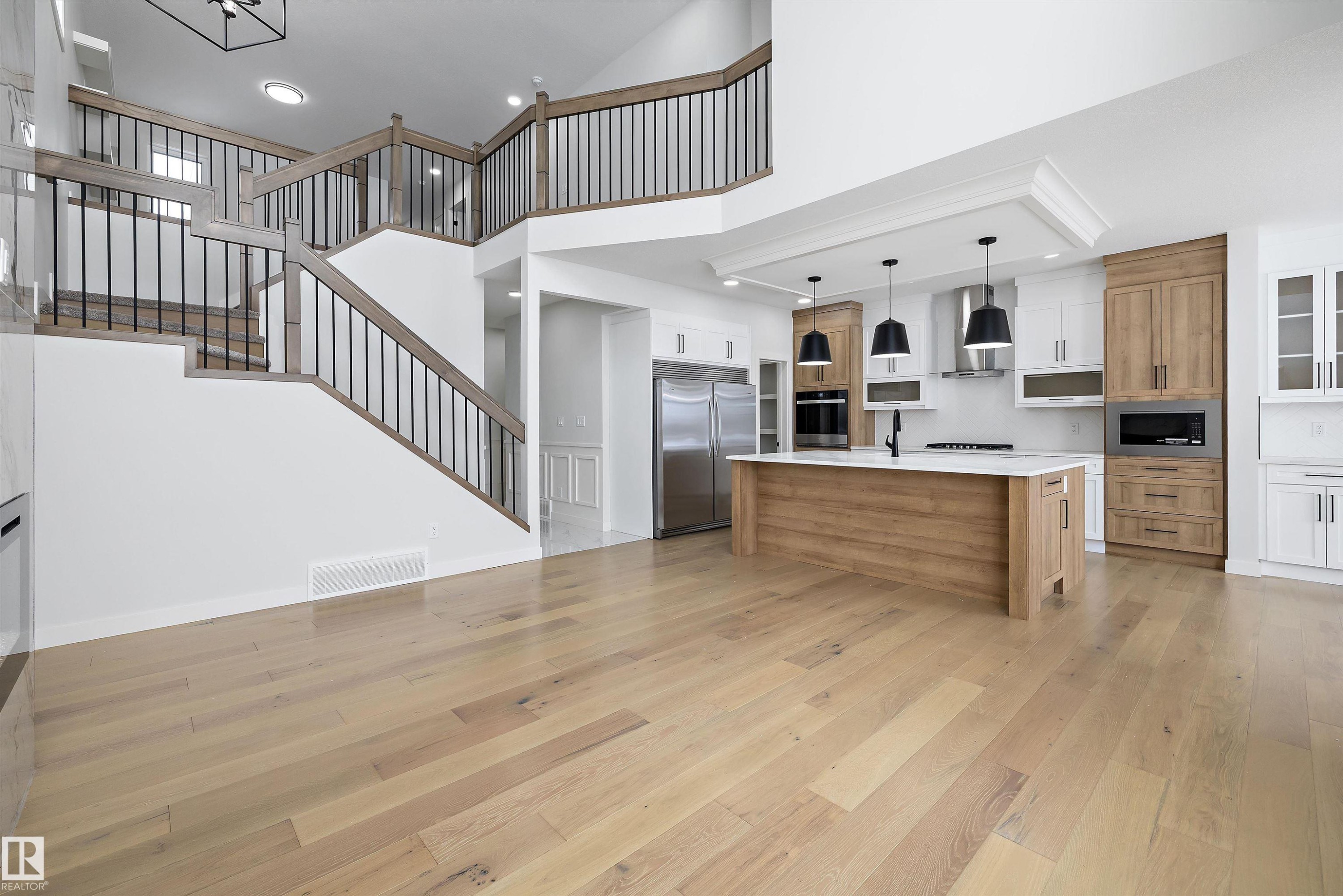 Dual tone kitchen featuring dual tone cabinetry, stainless steel fridge, open floor plan, pendant lighting, and light wood-style floors - 230 Edgemont Green Green Nw, Edmonton, AB - Indoor Photo Showing Kitchen