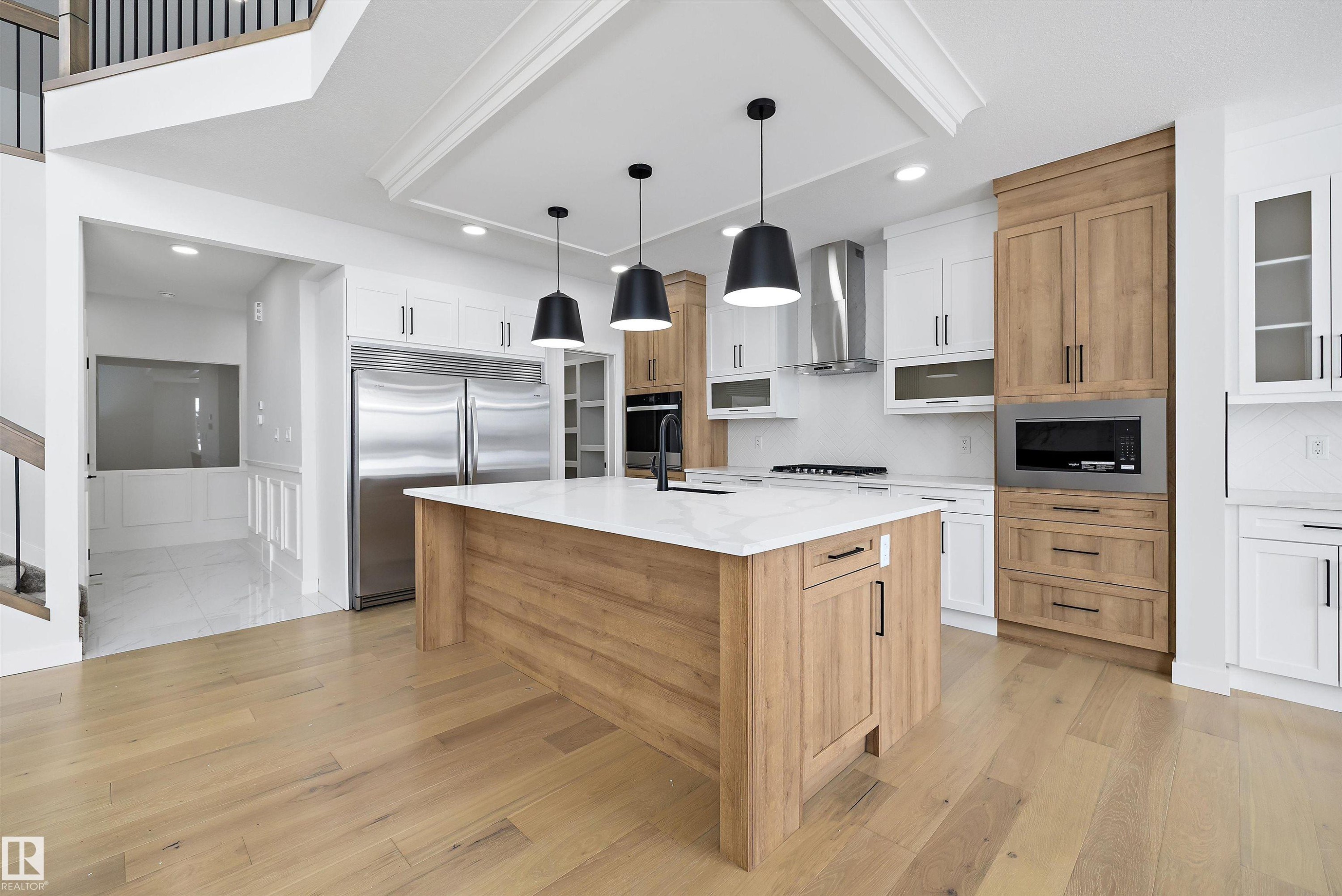 Kitchen with two tone cabinets, built in appliances, pendant lighting, light stone counters, and a kitchen island with sink - 230 Edgemont Green Green Nw, Edmonton, AB - Indoor Photo Showing Kitchen With Upgraded Kitchen