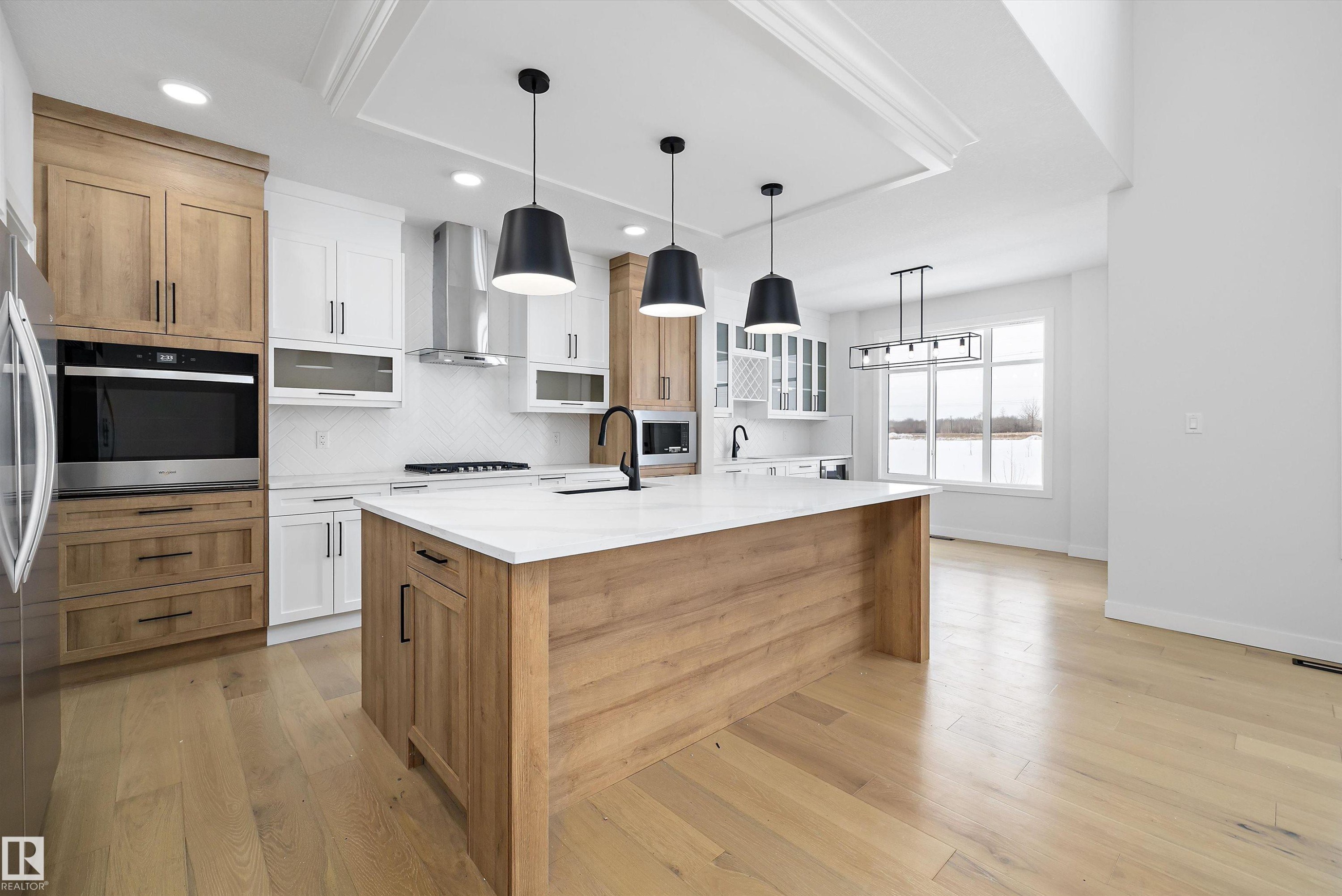 Dual tone kitchen featuring two tone cabinets, glass fronted cabinets, pendant lighting, light stone countertops, and light wood-type flooring - 230 Edgemont Green Green Nw, Edmonton, AB - Indoor Photo Showing Kitchen With Upgraded Kitchen