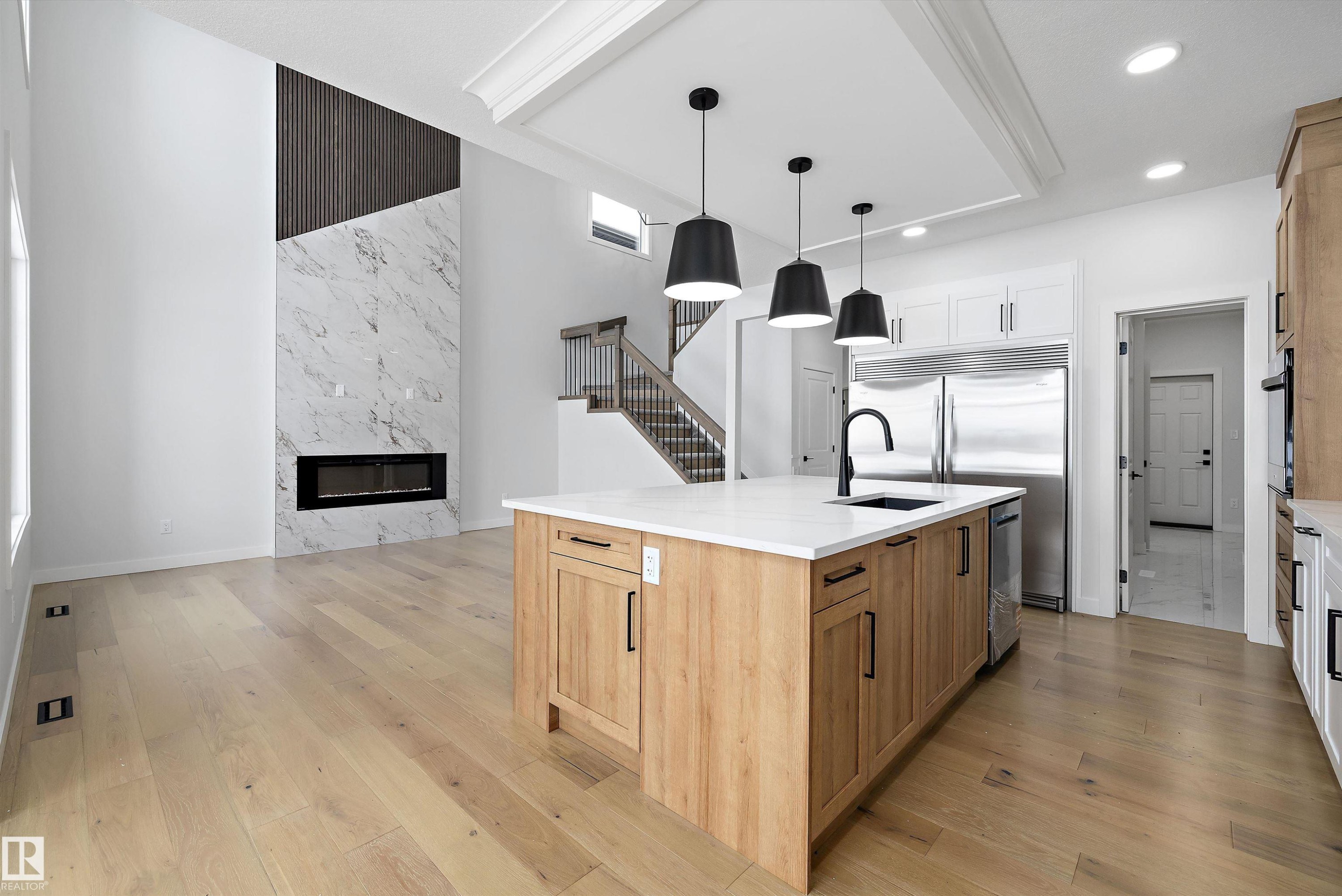 Dual tone kitchen featuring two tone color scheme, a high end fireplace, decorative light fixtures, an island with sink, and stainless steel appliances - 230 Edgemont Green Green Nw, Edmonton, AB - Indoor Photo Showing Kitchen With Upgraded Kitchen
