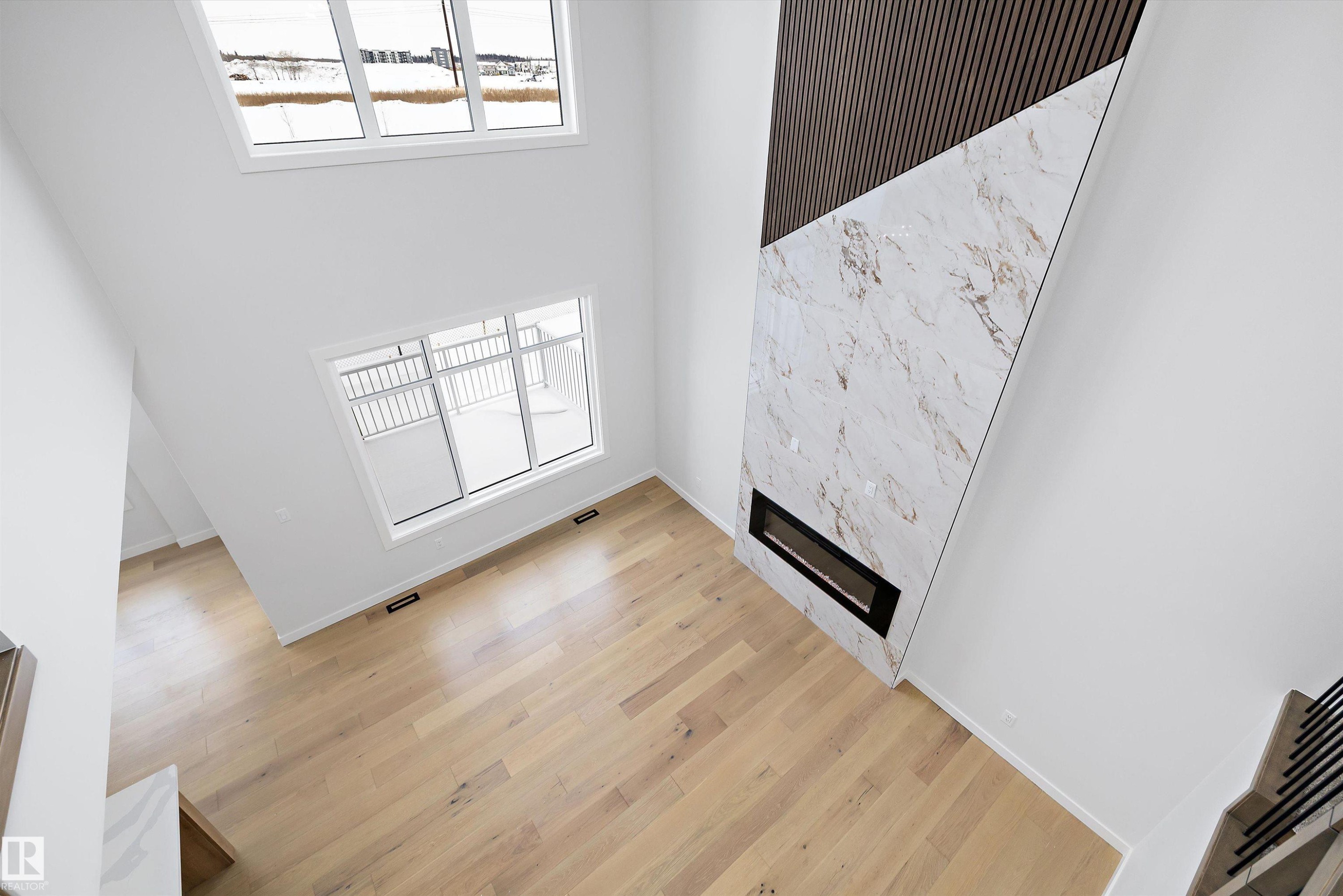 Unfurnished living room featuring healthy amount of natural light, a high ceiling, a premium fireplace, and light wood finished floors - 230 Edgemont Green Green Nw, Edmonton, AB - Indoor Photo Showing Other Room