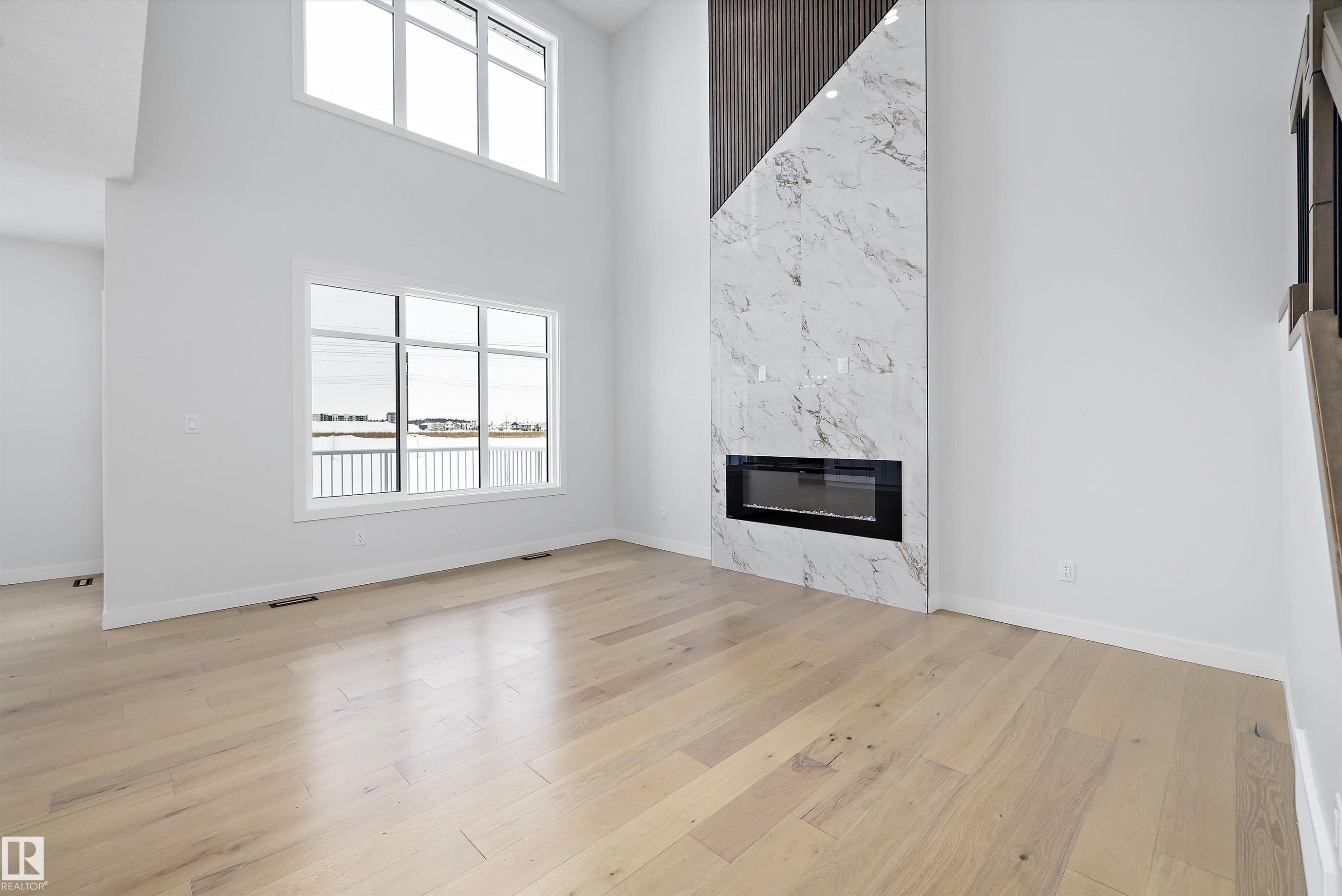 Unfurnished living room with a high ceiling, a high end fireplace, and light wood-type flooring - 230 Edgemont Green Green Nw, Edmonton, AB - Indoor With Fireplace