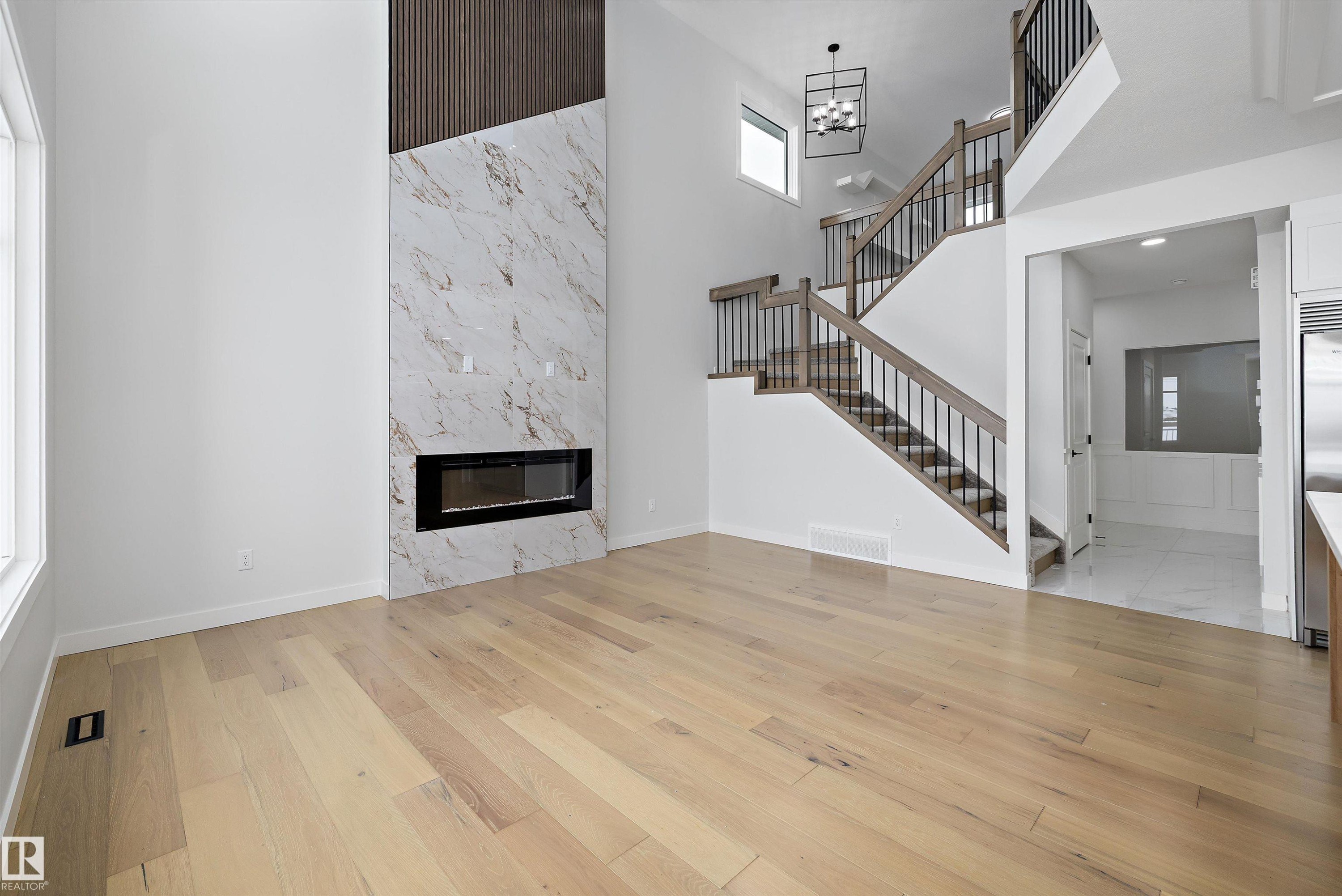 Unfurnished living room with a high end fireplace, a high ceiling, light wood-style floors, and suspended lighting - 230 Edgemont Green Green Nw, Edmonton, AB - Indoor With Fireplace