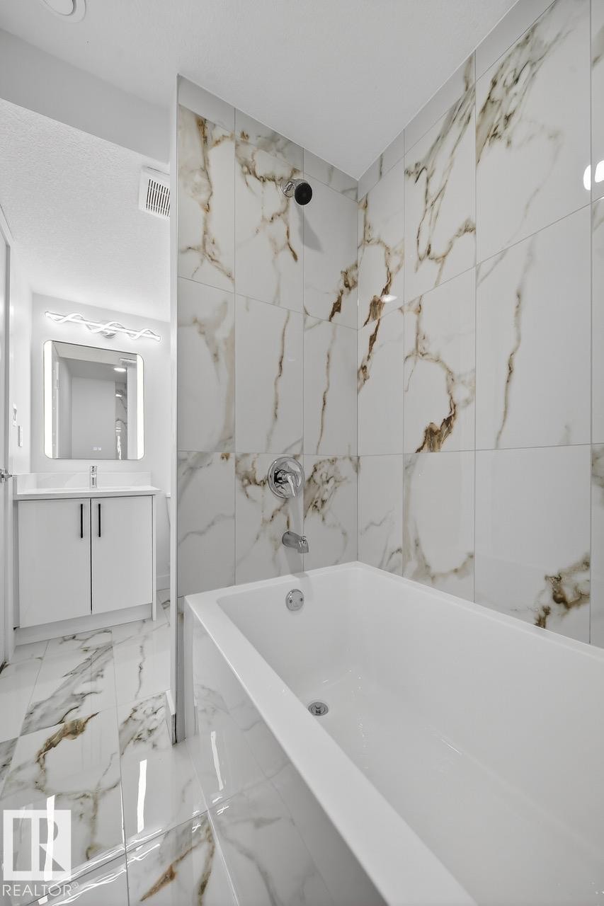 Bathroom featuring vanity, bathtub / shower combination, and light marble finish floors - 12919 113A Street, Edmonton, AB - Indoor Photo Showing Bathroom