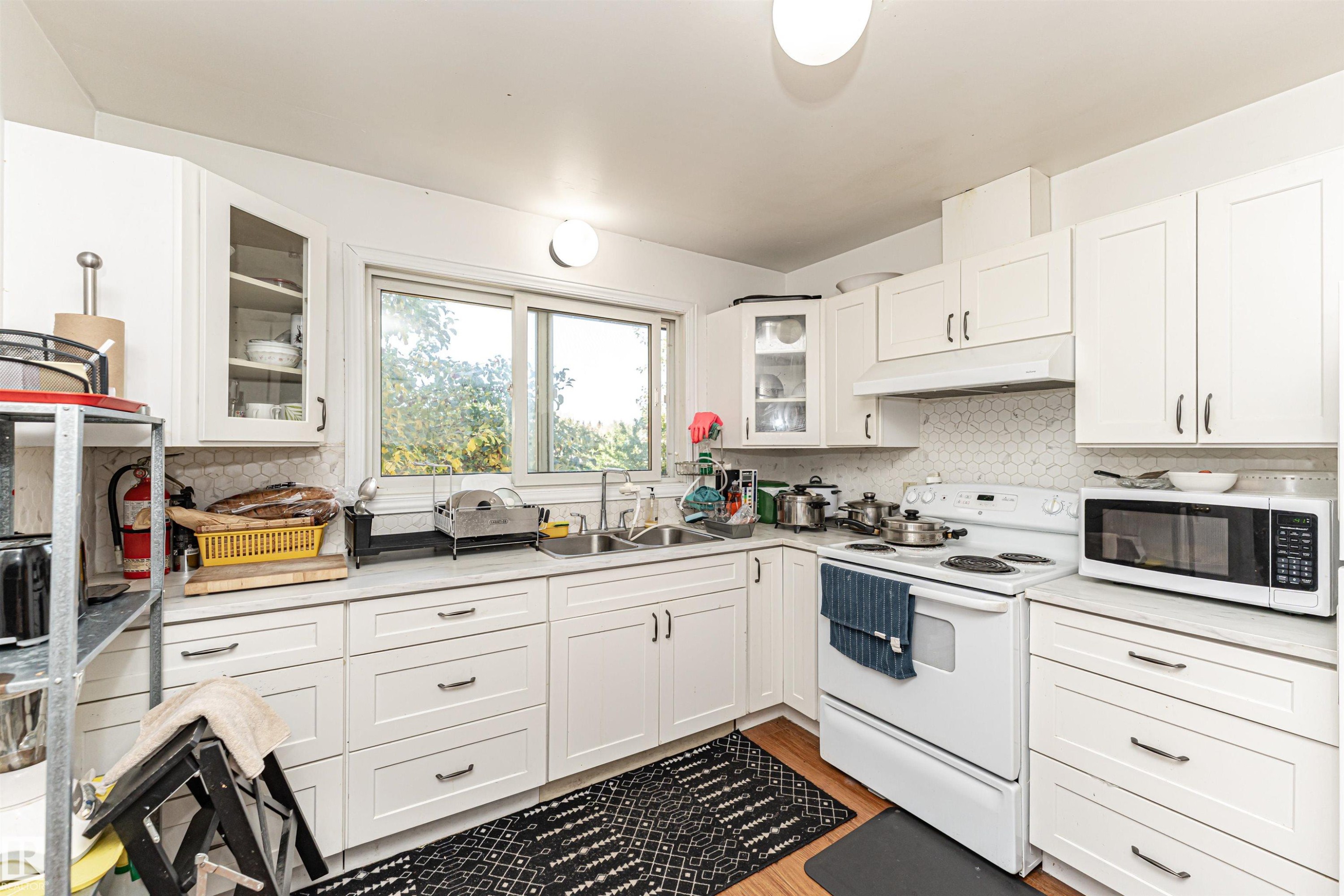 Kitchen with white appliances, white cabinets, glass insert cabinets, and under cabinet range hood - 2349 Millbourne Road W, Edmonton, AB - Indoor Photo Showing Kitchen With Double Sink