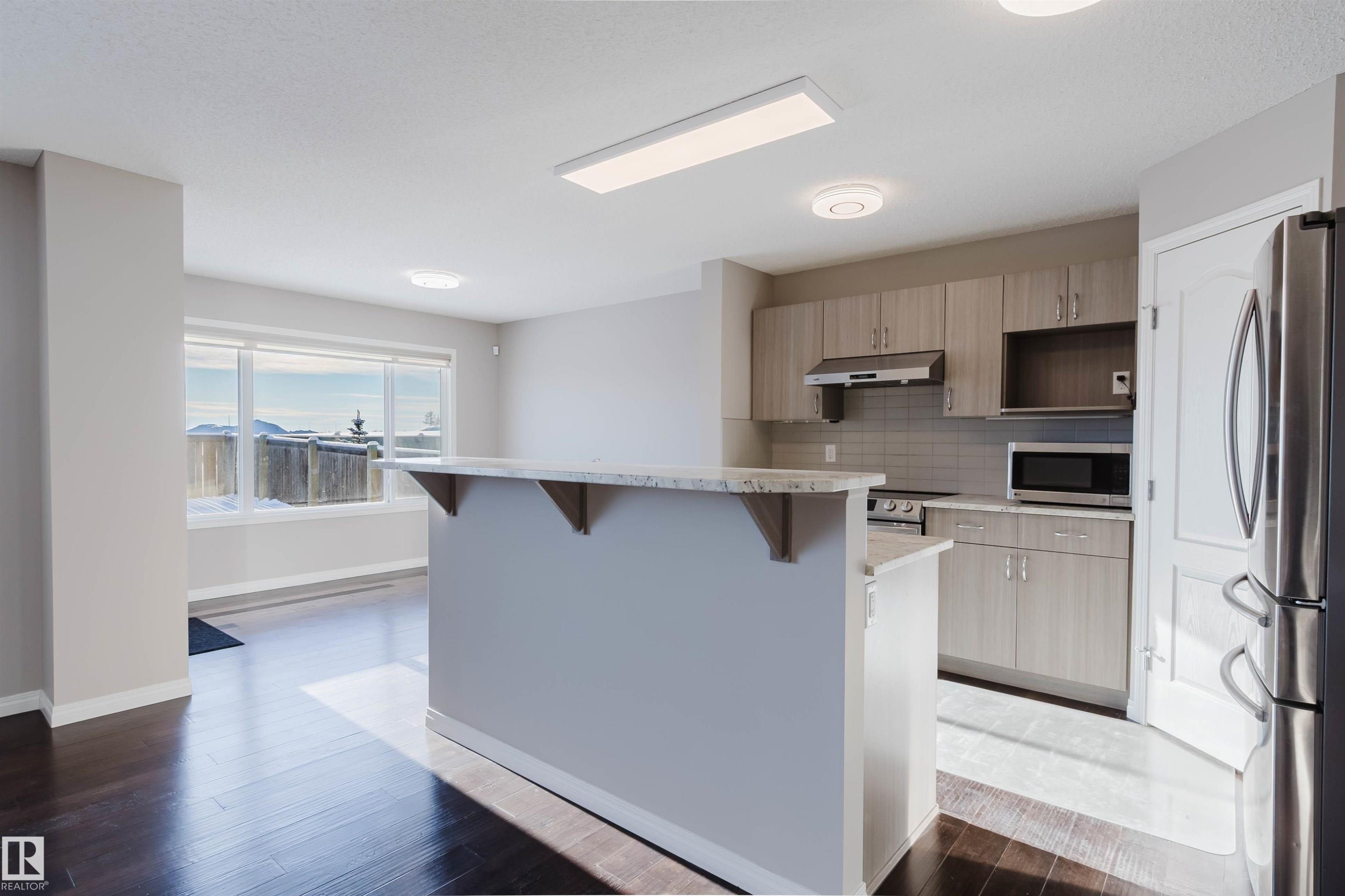 Kitchen featuring appliances with stainless steel finishes, a breakfast bar area, tasteful backsplash, light stone countertops, and dark wood finished floors - 16627 18 Avenue, Edmonton, AB - Indoor Photo Showing Kitchen
