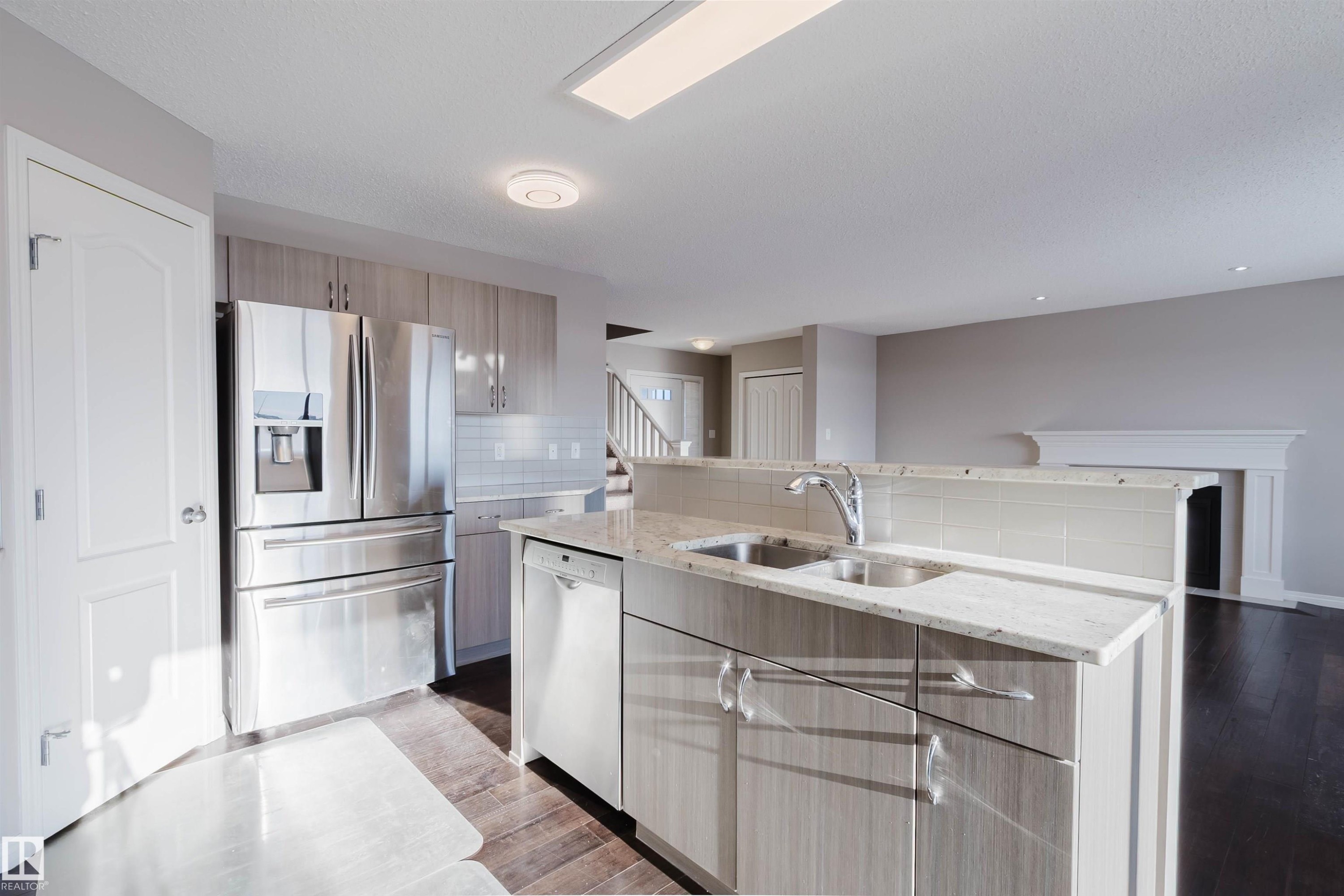 Kitchen with light stone countertops, appliances with stainless steel finishes, decorative backsplash, an island with sink, and light wood finished floors - 16627 18 Avenue, Edmonton, AB - Indoor Photo Showing Kitchen With Double Sink