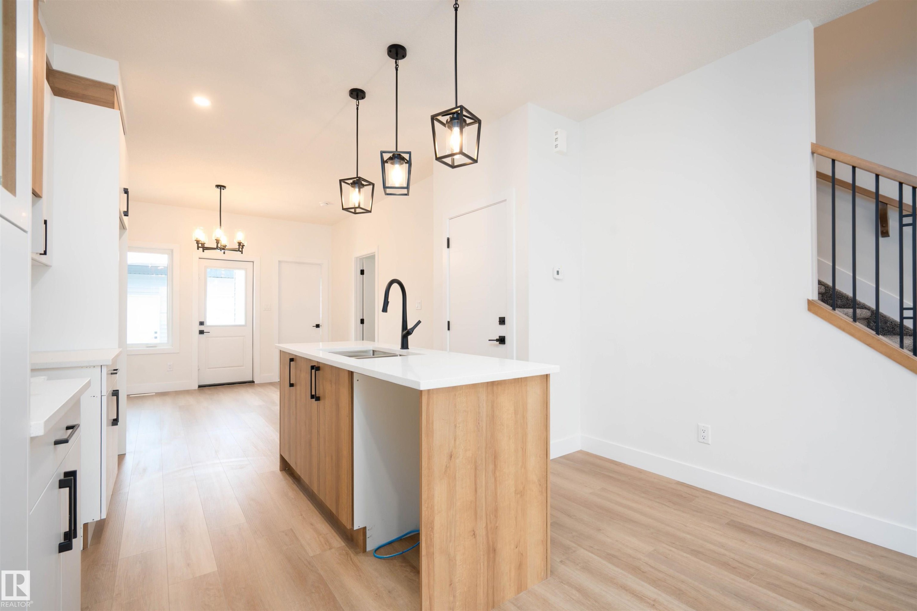 Kitchen with white cabinetry, a center island with sink, pendant lighting, and light wood finished floors - 430 Crystal Creek Link, Leduc, AB - Indoor Photo Showing Kitchen