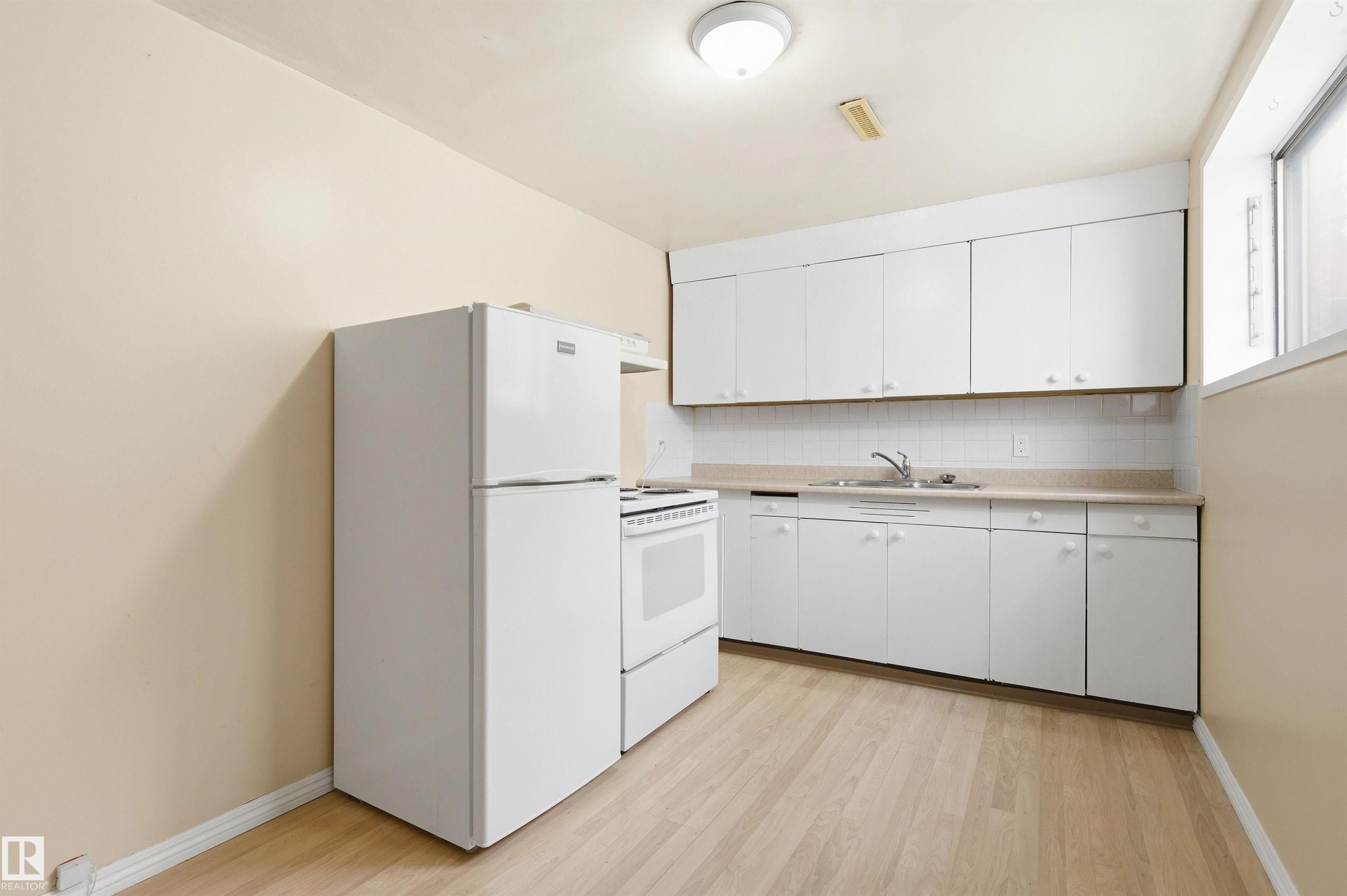 Kitchen featuring white appliances, light countertops, white cabinets, light wood finished floors, and decorative backsplash - 10332 82 Street, Edmonton, AB - Indoor Photo Showing Kitchen