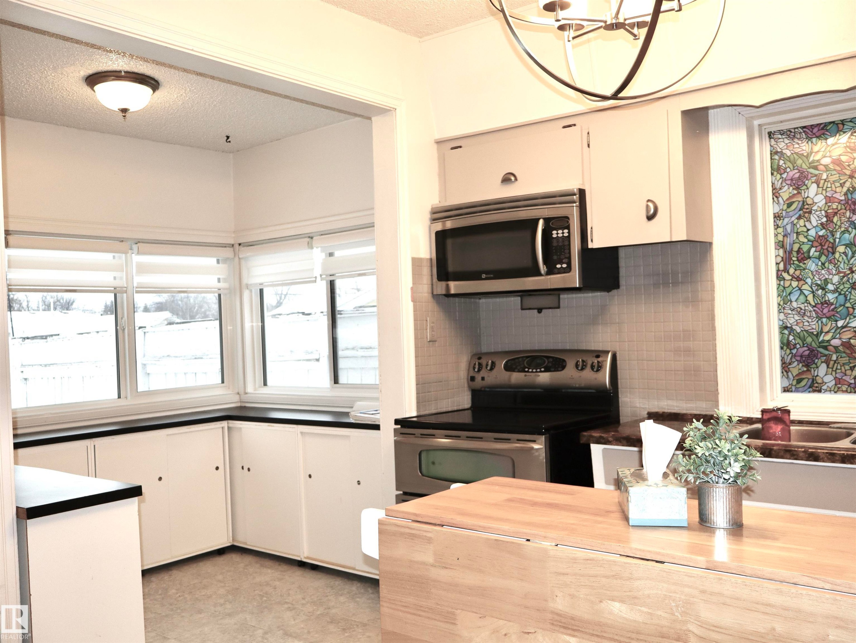 Kitchen with appliances with stainless steel finishes, a textured ceiling, white cabinetry, tasteful backsplash, and a chandelier - 4511 53 Ave, Barrhead, AB - Indoor Photo Showing Kitchen