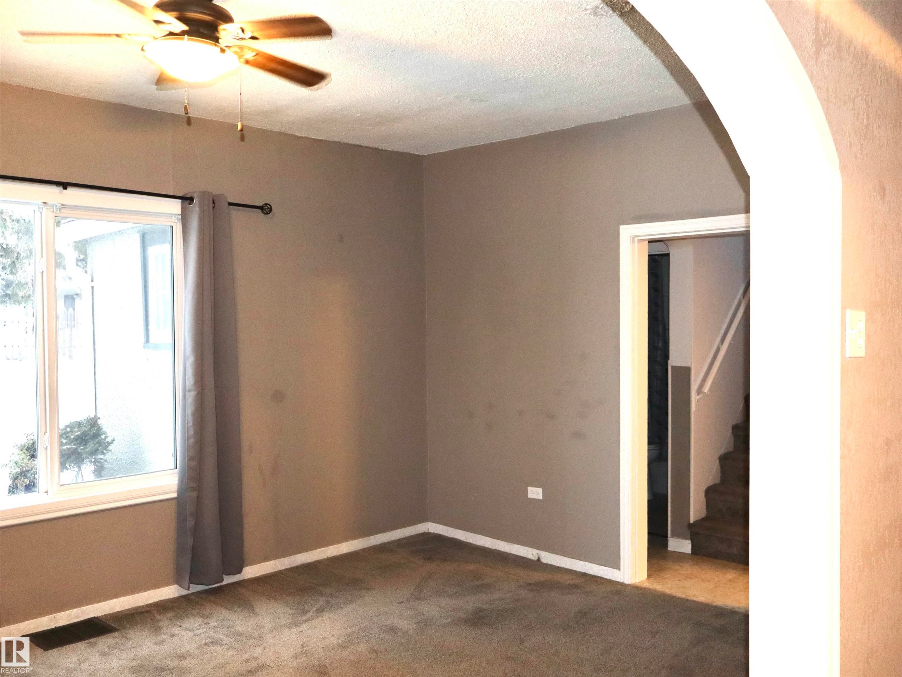 Unfurnished room featuring dark colored carpet, ceiling fan, arched walkways, stairs, and a textured ceiling - 4511 53 Ave, Barrhead, AB - Indoor Photo Showing Other Room