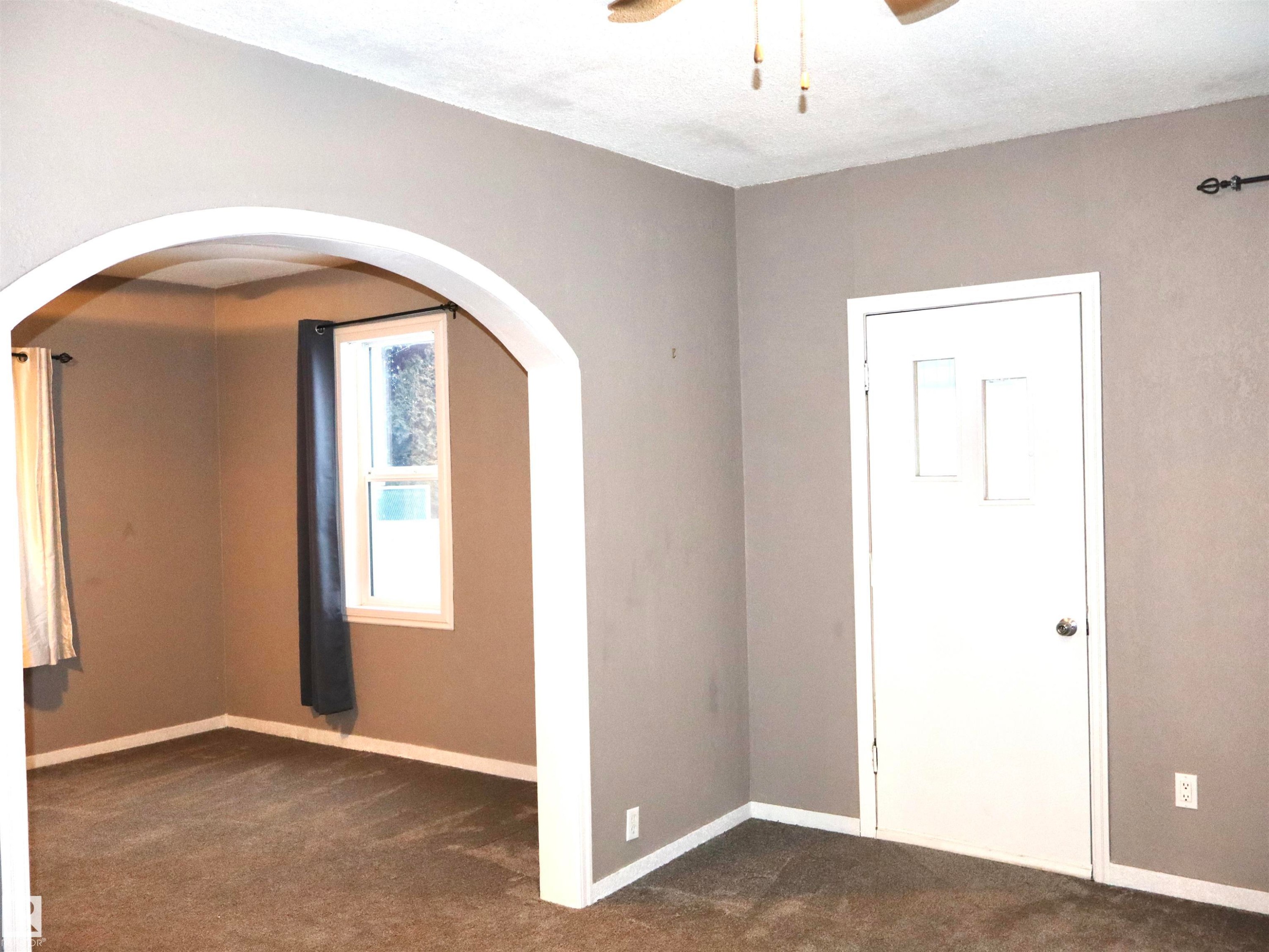 Unfurnished room with dark colored carpet, arched walkways, and a ceiling fan - 4511 53 Ave, Barrhead, AB - Indoor Photo Showing Other Room