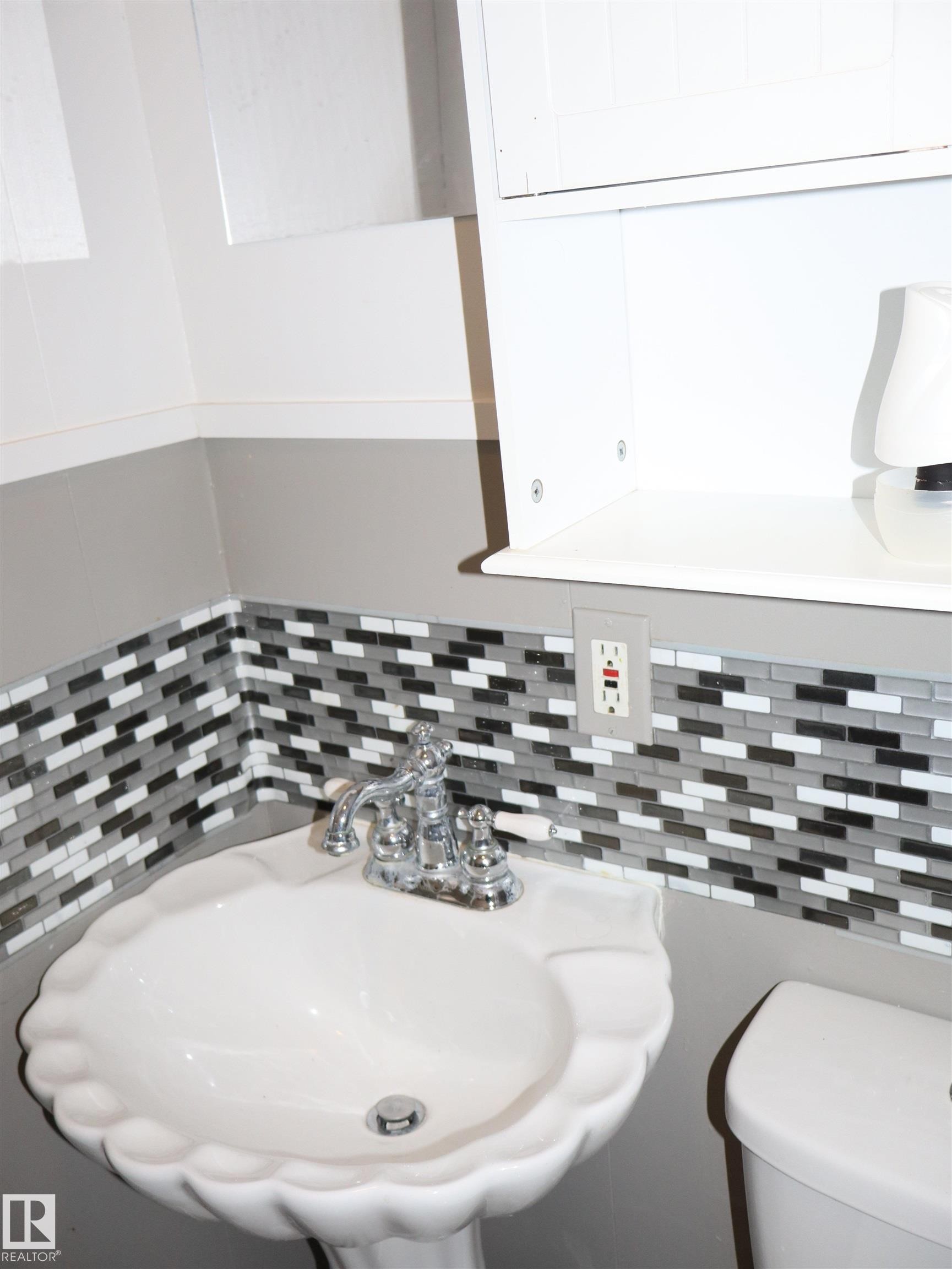 Half bathroom featuring a sink and decorative backsplash - 4511 53 Ave, Barrhead, AB - Indoor Photo Showing Bathroom