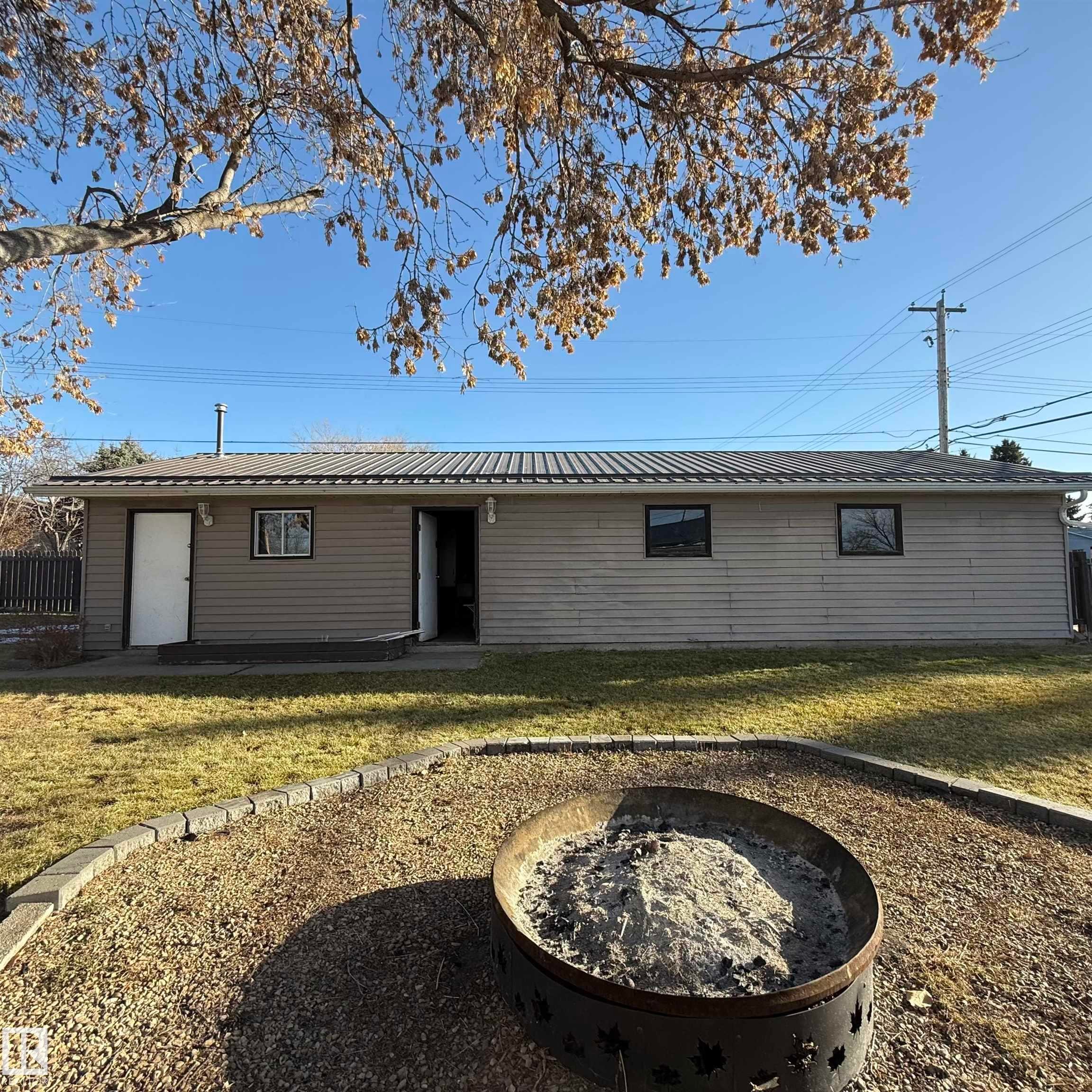Rear view of house featuring a fire pit, a lawn, and a metal roof - 4511 53 Ave, Barrhead, AB - Outdoor