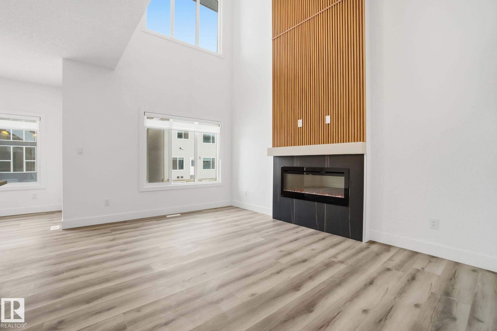 Unfurnished living room featuring a glass covered fireplace, a high ceiling, plenty of natural light, and light wood-style floors - 2532 210 Street, Edmonton, AB - Indoor Photo Showing Living Room With Fireplace