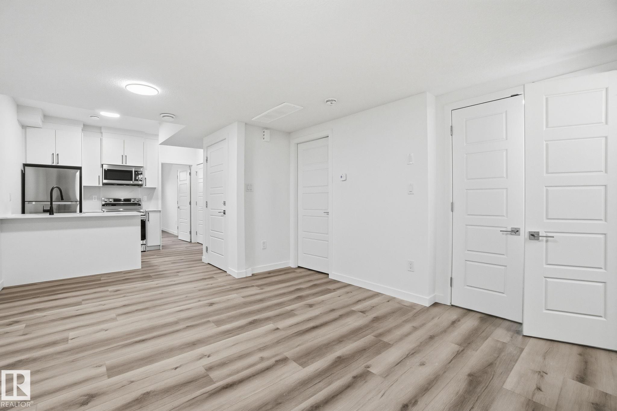 Kitchen with white cabinetry, light countertops, stainless steel appliances, light wood finished floors, and open floor plan - 2532 210 Street, Edmonton, AB - Indoor Photo Showing Kitchen