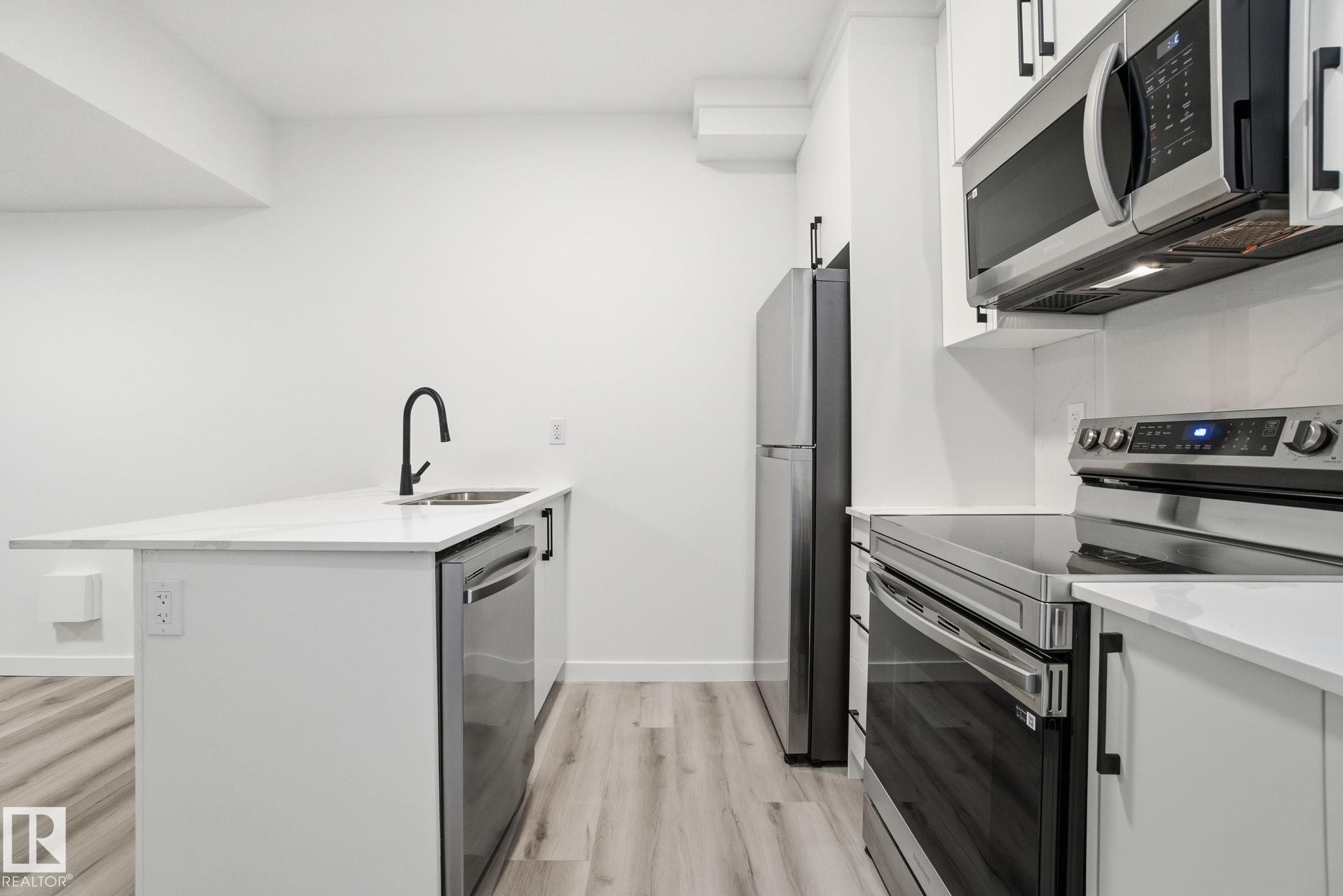 Kitchen featuring stainless steel appliances, a peninsula, light wood-style flooring, white cabinets, and light stone countertops - 2532 210 Street, Edmonton, AB - Indoor Photo Showing Kitchen