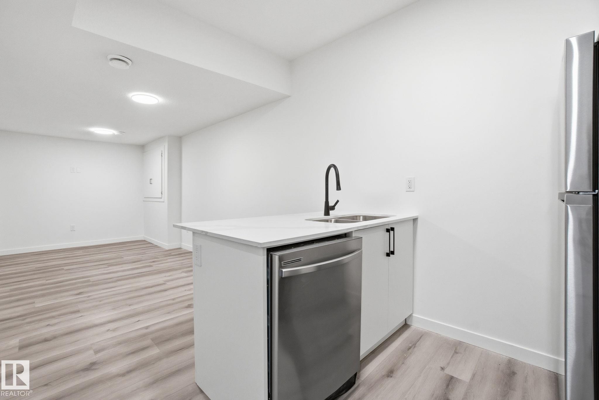 Kitchen with white cabinets, appliances with stainless steel finishes, a peninsula, light wood-type flooring, and light stone countertops - 2532 210 Street, Edmonton, AB - Indoor