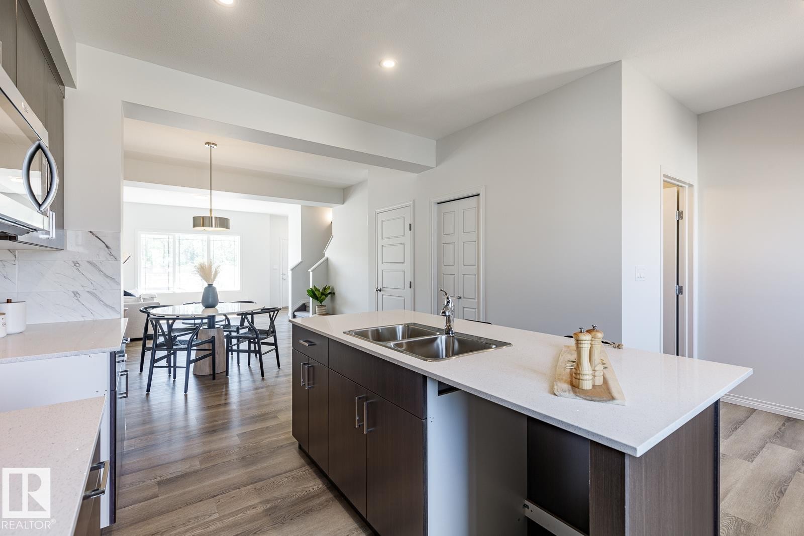 Kitchen featuring dark brown cabinetry, stainless steel appliances, hanging light fixtures, decorative backsplash, and an island with sink - 3617 Triomphe Boulevard, Beaumont, AB - Indoor Photo Showing Kitchen With Double Sink With Upgraded Kitchen