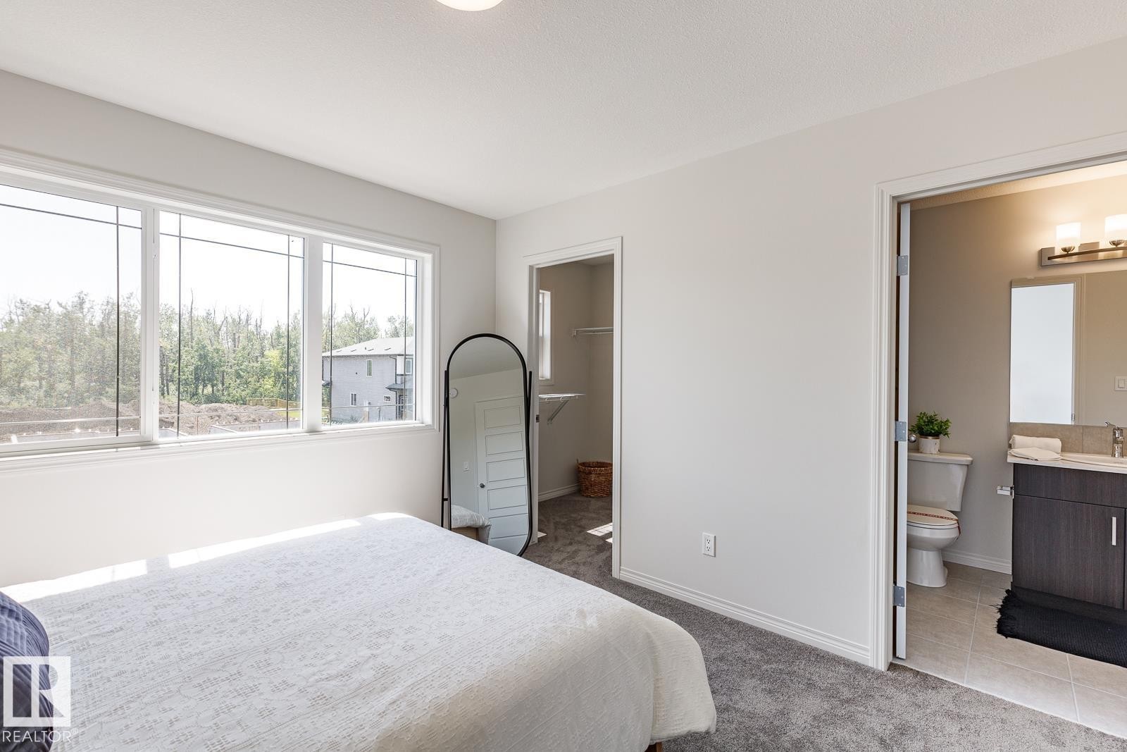 Bedroom featuring light colored carpet, connected bathroom, a spacious closet, and light tile patterned floors - 3617 Triomphe Boulevard, Beaumont, AB - Indoor Photo Showing Bedroom