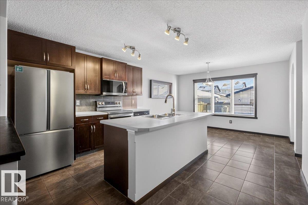 Kitchen featuring stainless steel appliances, dark brown cabinets, light countertops, an island with sink, and a textured ceiling - 3623 13 Street, Edmonton, AB - Indoor Photo Showing Kitchen With Double Sink
