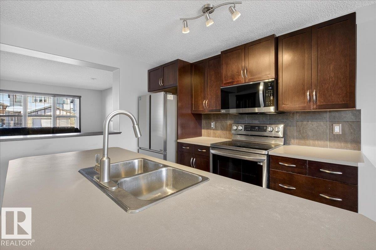 Kitchen with stainless steel appliances, backsplash, light countertops, dark brown cabinets, and a textured ceiling - 3623 13 Street, Edmonton, AB - Indoor Photo Showing Kitchen With Double Sink