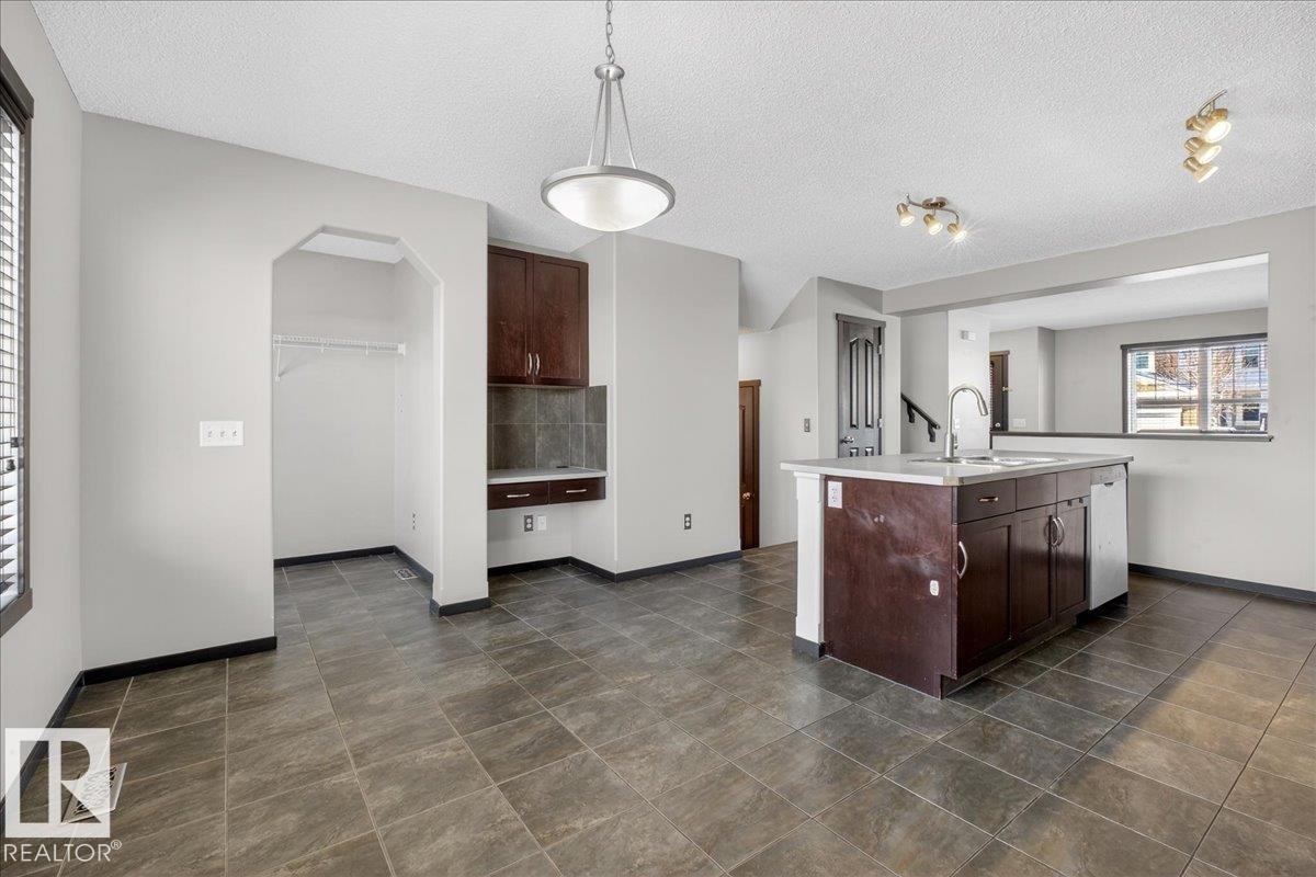 Kitchen featuring dark brown cabinetry, a textured ceiling, hanging light fixtures, a kitchen island with sink, and dishwasher - 3623 13 Street, Edmonton, AB - Indoor Photo Showing Kitchen