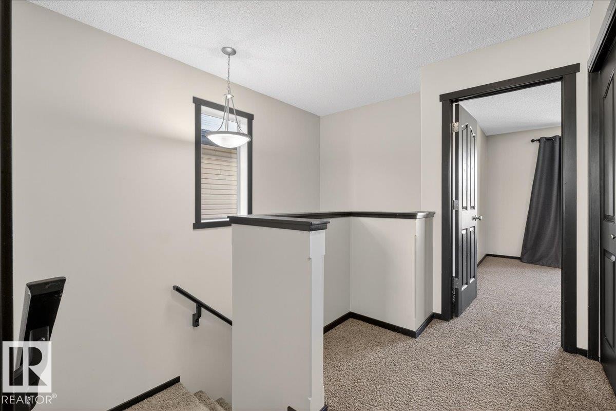 Hall with an upstairs landing, light colored carpet, and a textured ceiling - 3623 13 Street, Edmonton, AB - Indoor